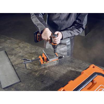 Een persoon gebruikt een oranje boormachine op een metalen stuk dat is vastgeklemd in een bankschroef. Op de tafel staat een oranje gereedschapskist.