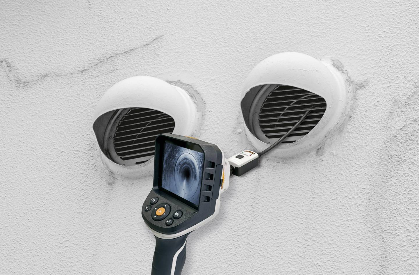Een inspectiecamera wordt gebruikt voor onderzoek naar ventilatiekanalen in een witte muur. Het scherm toont een binnenaanzicht.