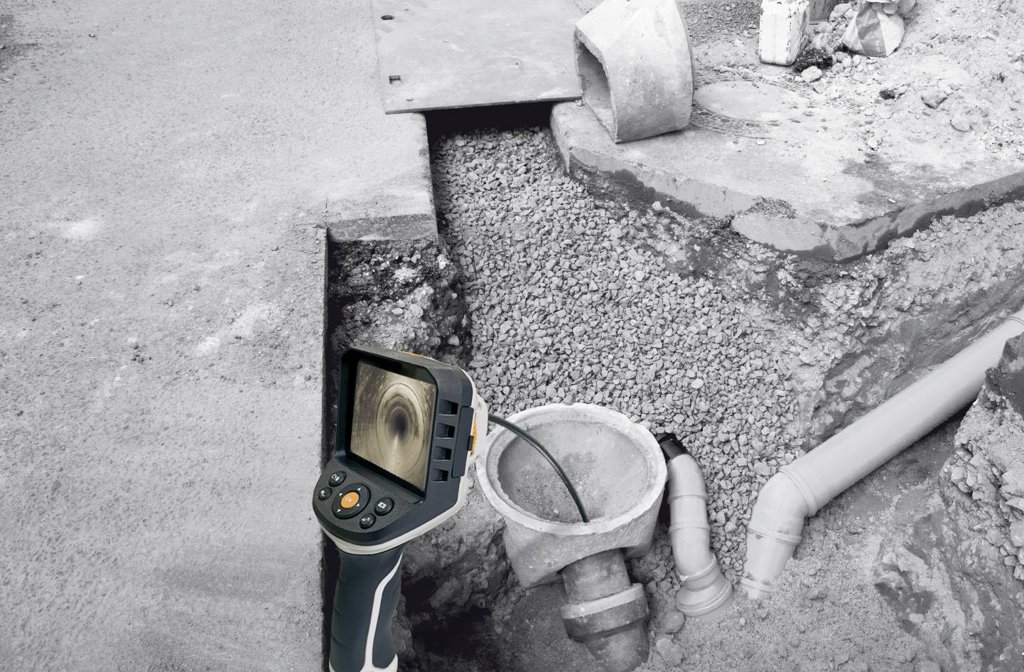 Een inspectiecamera onderzoekt een ondergrondse pijpleiding. Op het scherm is de binnenkant van een buis te zien. Grind omringt de buizen.
