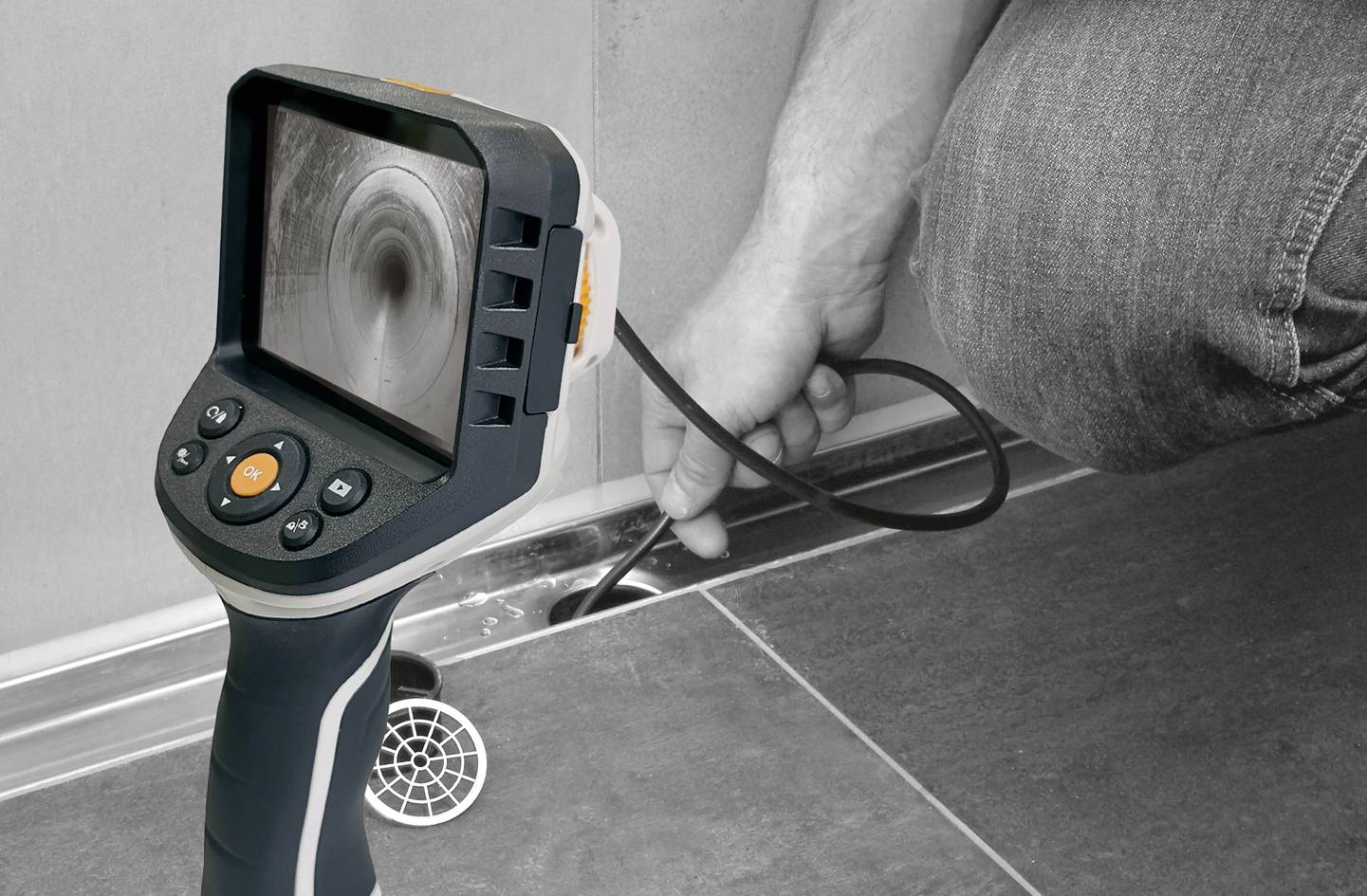 Een persoon inspecteert een afvoer met een inspectiecamera. Het camerbeeld toont het binnenste van de buis.