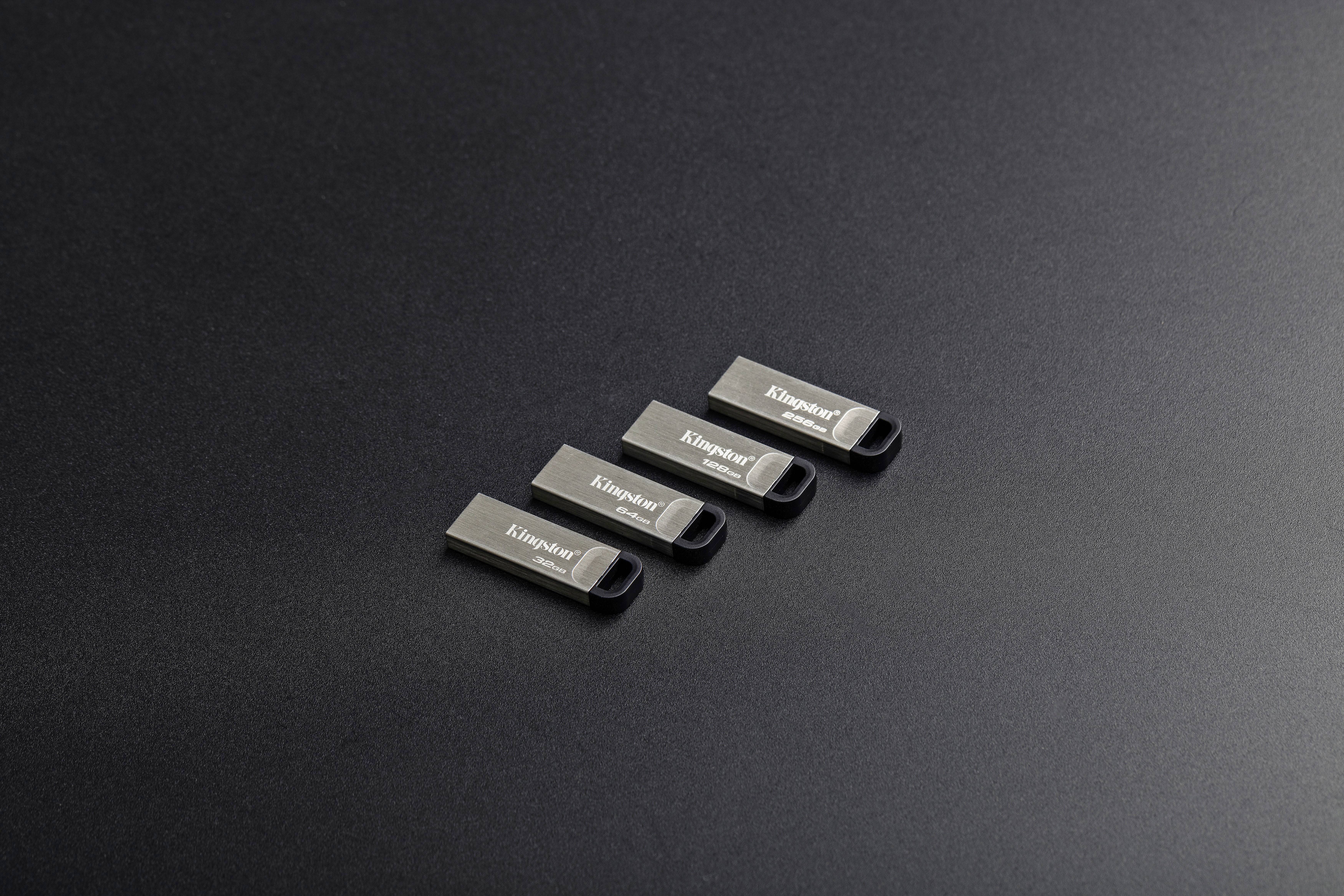 Vier grijze USB-sticks met het opschrift 'Kingston' liggen naast elkaar op een zwarte achtergrond.
