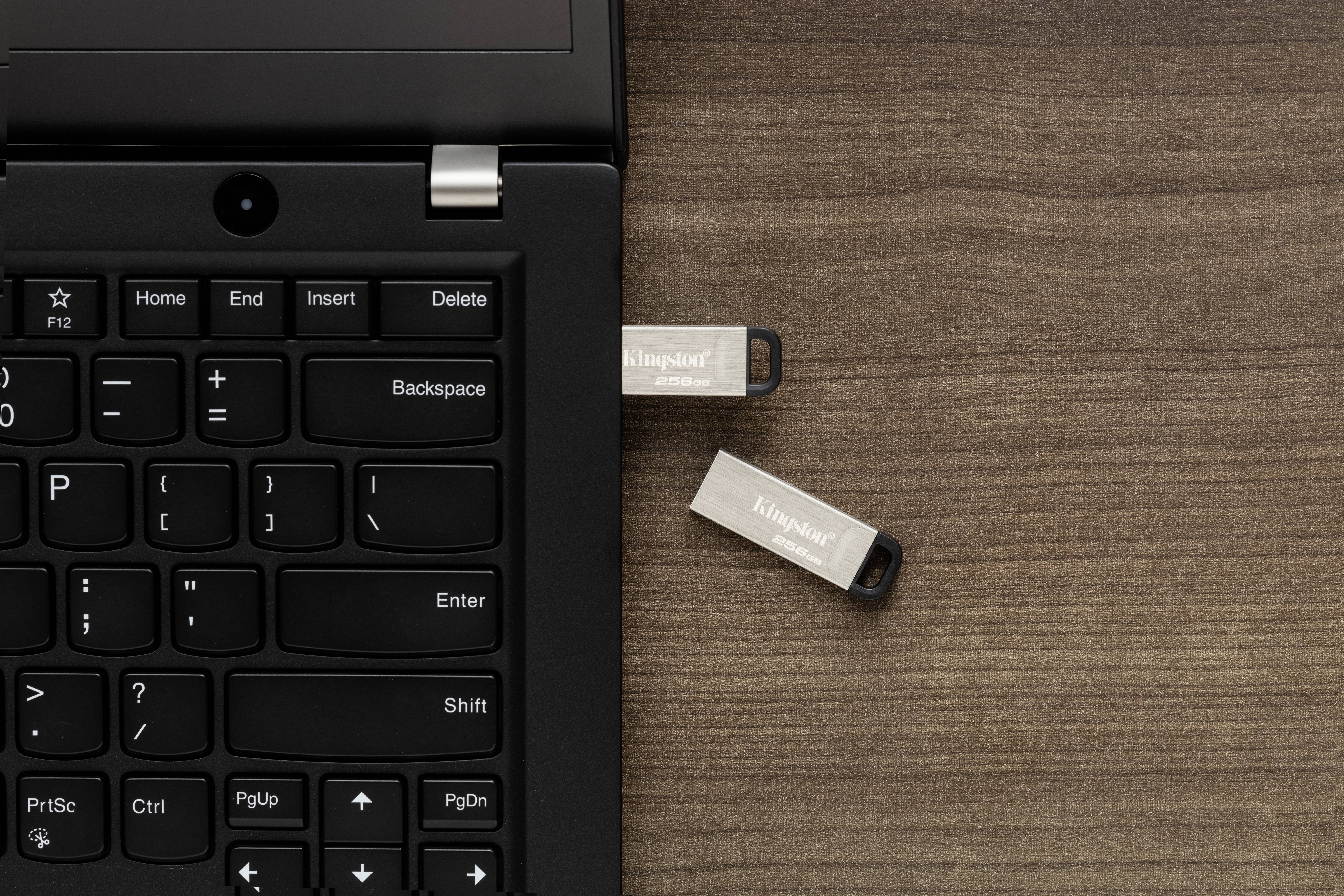 Een zwarte laptop met een USB-toetsenbord, waar twee USB-sticks in zijn gestoken, ligt op een houten tafel.
