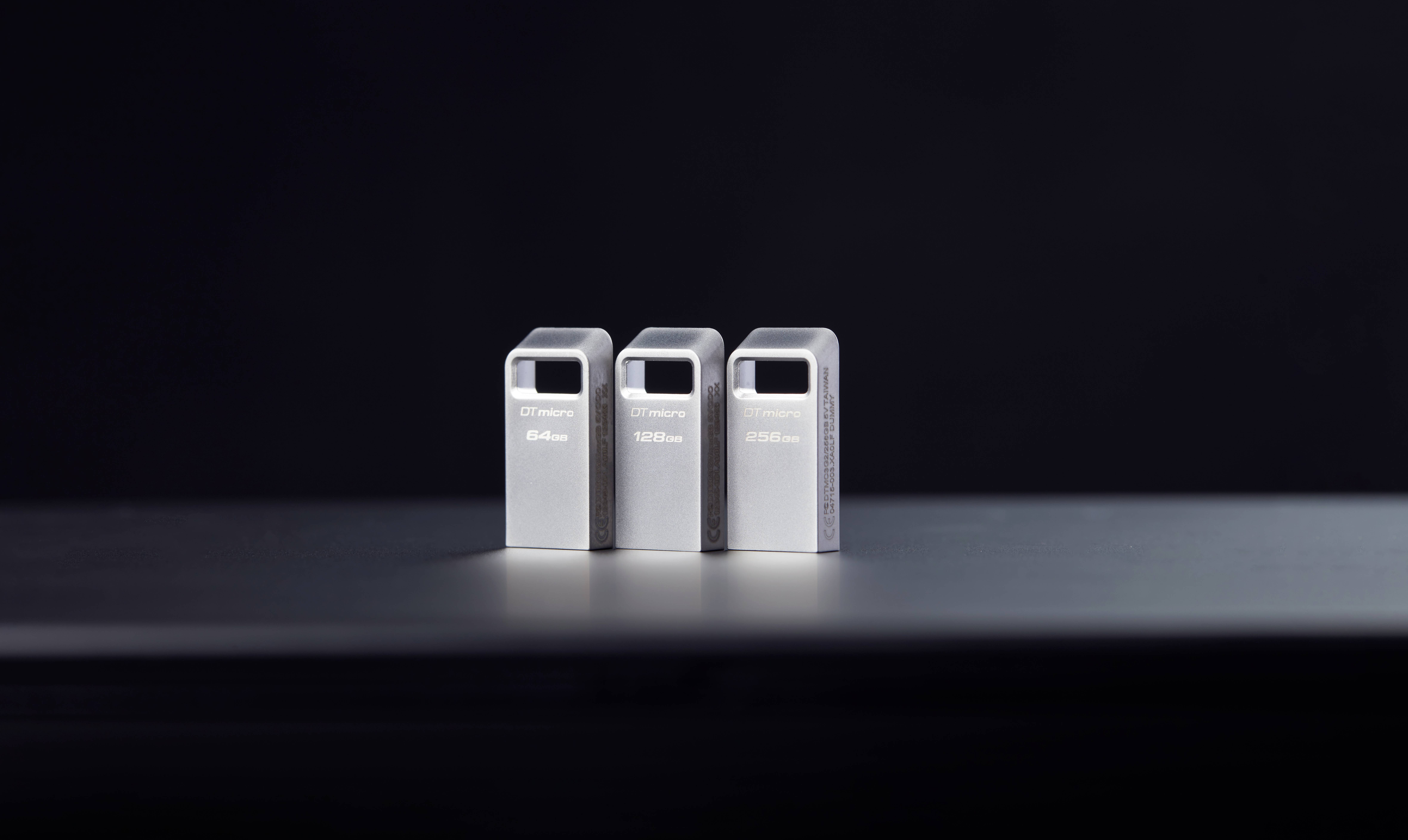 Drie zilveren USB-drives staan naast elkaar op een donker oppervlak voor een zwarte achtergrond.