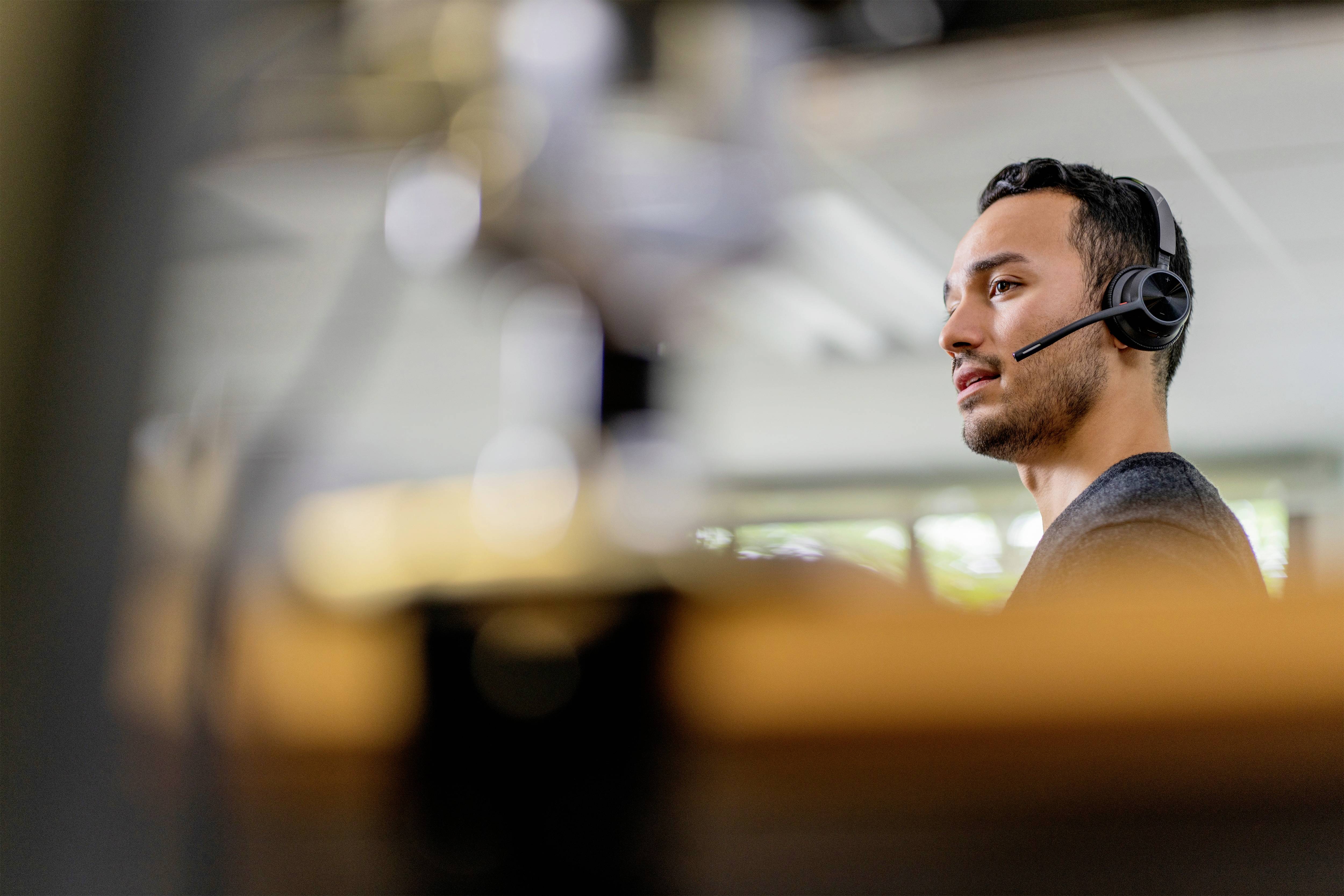Man met headset op kantoor, geconcentreerd aan het werk op de computer. Hij belt of neemt deel aan een virtuele vergadering.