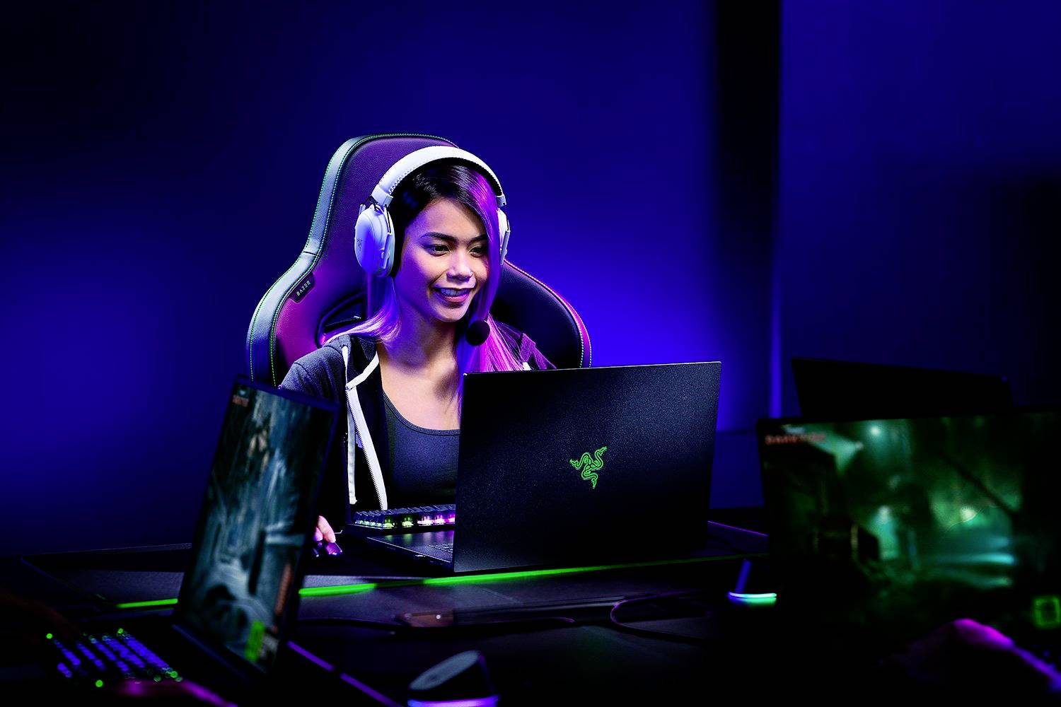 Een persoon speelt op een gaming-laptop, draagt een headset en zit op een gamingstoel. De omgeving is donker met blauw licht.