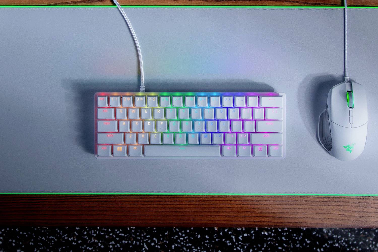 Toetsenbord met regenboogverlichting en witte muis op een grijs muismat, omrand met groen, op een houten oppervlak.