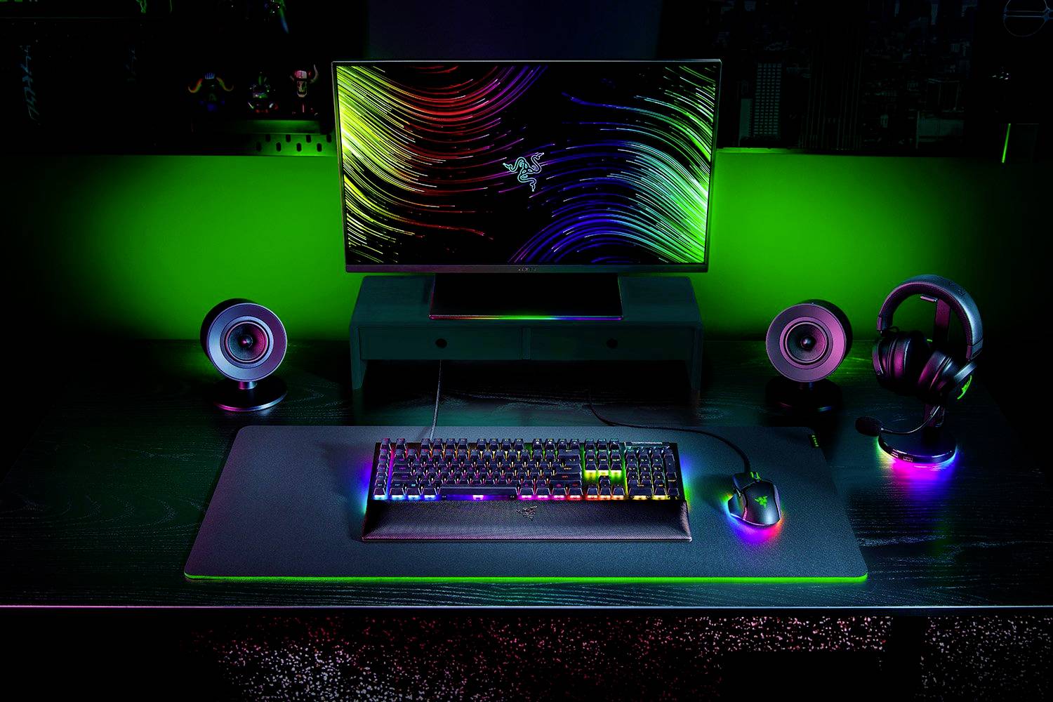 Een bureau met gaming-apparatuur: monitor toont kleurrijke graphics, verlicht toetsenbord, muis, speakers en koptelefoon onder neonverlichting.