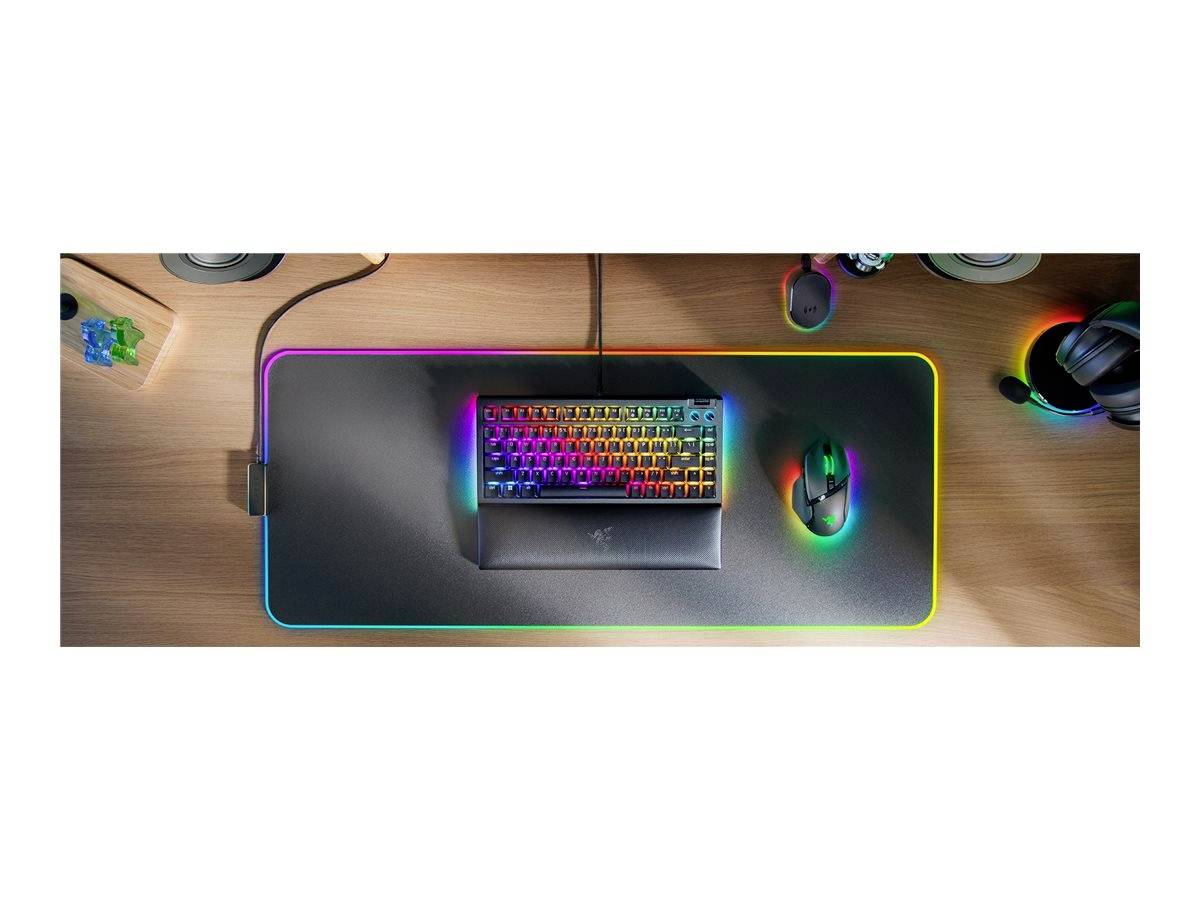 Kleurrijk RGB-toetsenbord en muis op een groot muismat, op een houten bureau. Koptelefoon en speakers wijzen op een gamingopstelling.