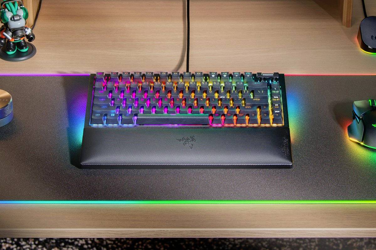 Toetsenbord op bureau met regenboog-achtergrondverlichting, naast een muis en speelfiguur.