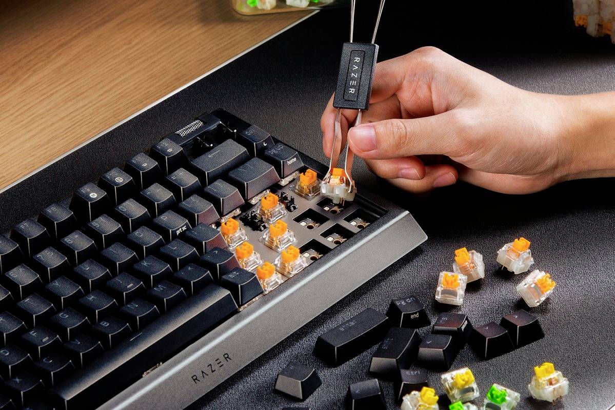 Een hand verwisselt mechanische toetsen op een toetsenbord. Verschillende toetsen zijn verwijderd. Op de voorgrond liggen verwijderde schakelaars.