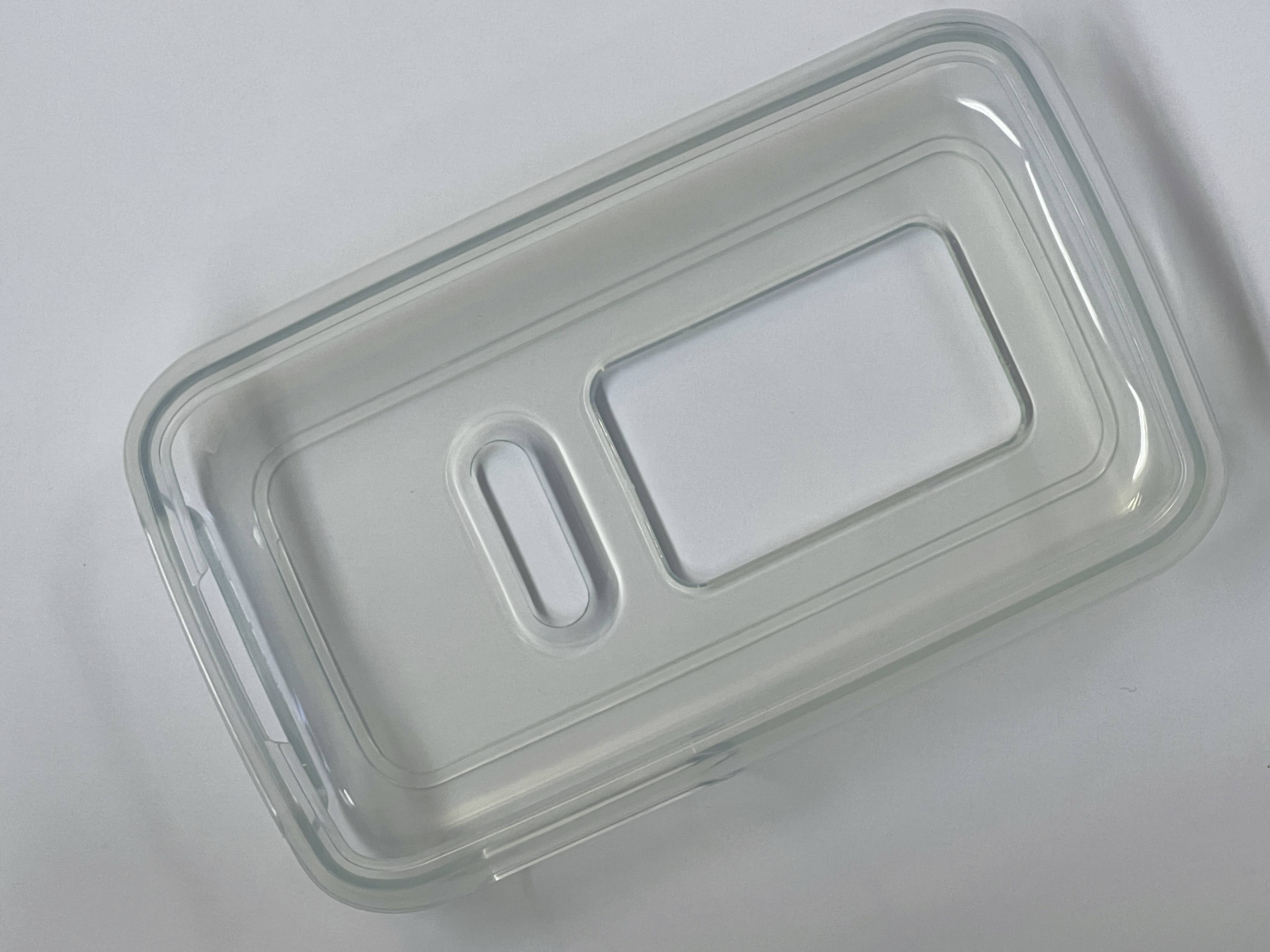 Een rechthoekige, transparante plastic deksel met twee rechthoekige uitsneden ligt op een grijze ondergrond.