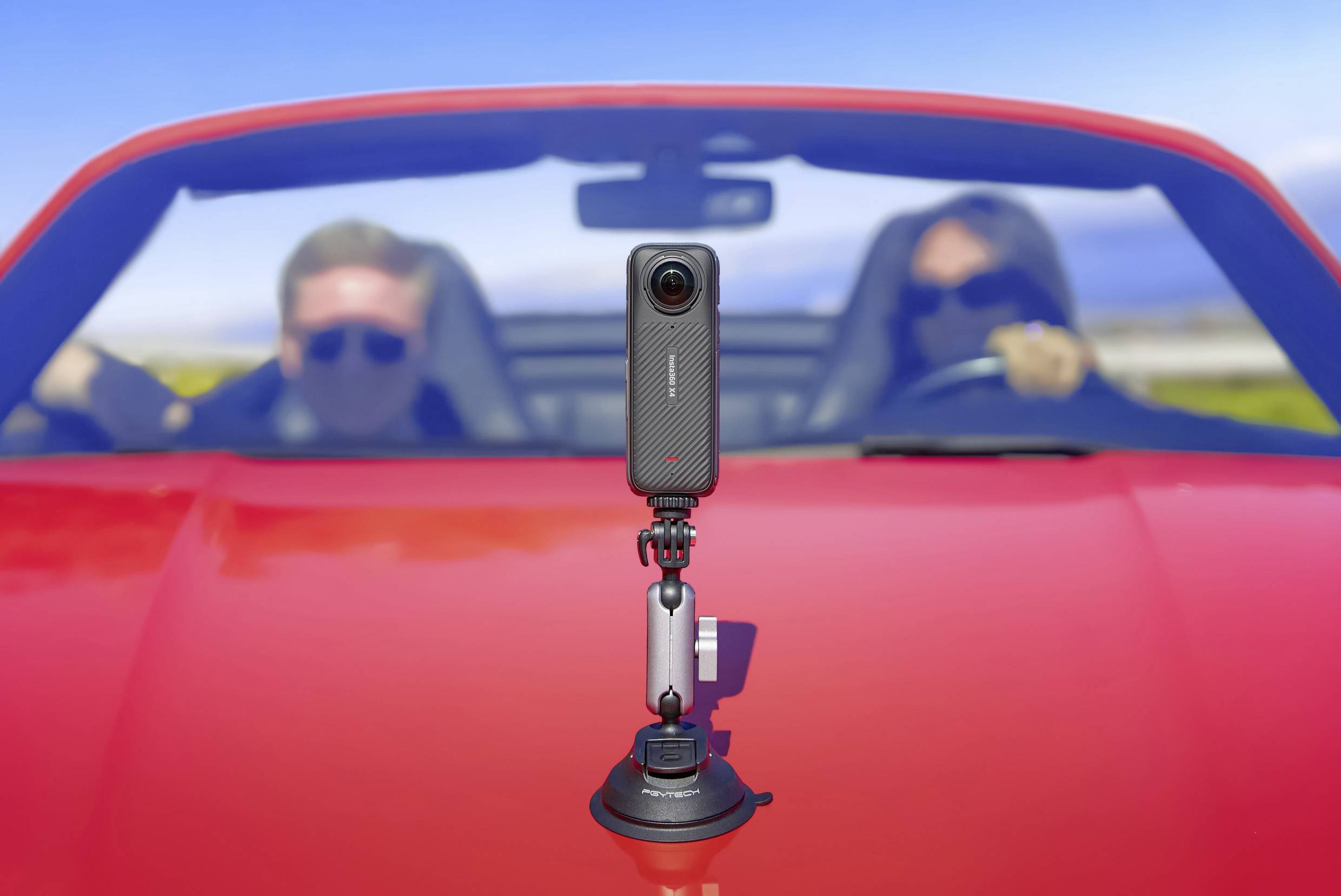Een camera is gemonteerd op een rode cabrio waarin twee personen zitten. De camera staat scherp, terwijl de personen wazig zijn.