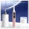 Elektrische tandenborstel in roze met een ronde borstenkop, staand naast een witte lotion fles; moderne badkameromgeving.