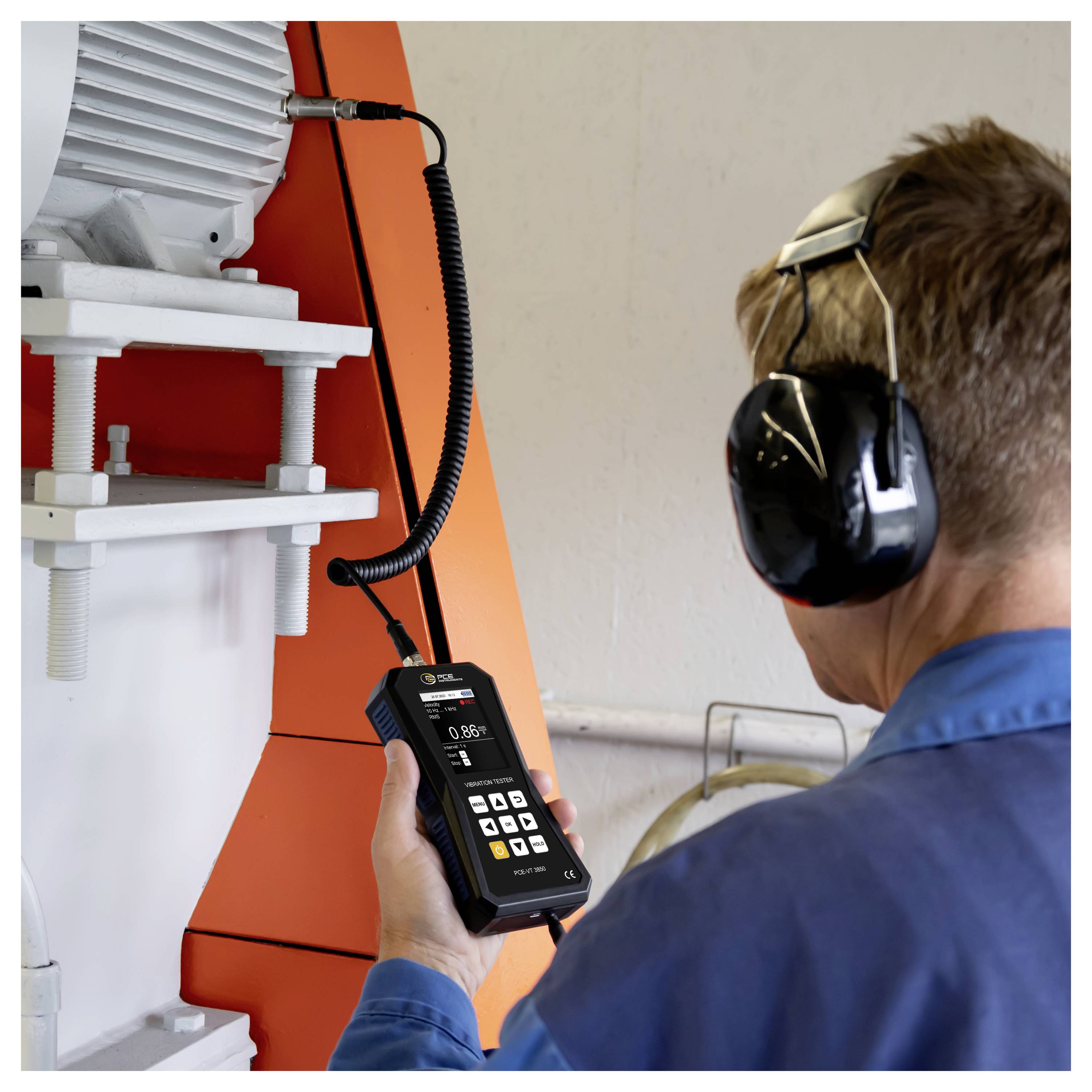 Technicus die gehoorbescherming draagt, gebruikt een handheld meter om industriële machines in een werkplaats te inspecteren.