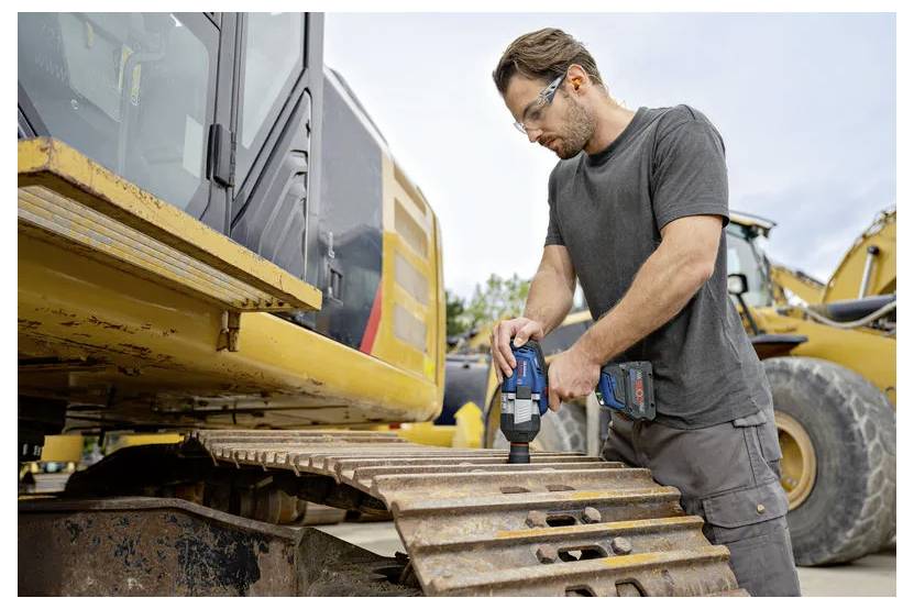 Man die een boormachine gebruikt om een houten balk op een bouwplaats vast te schroeven.