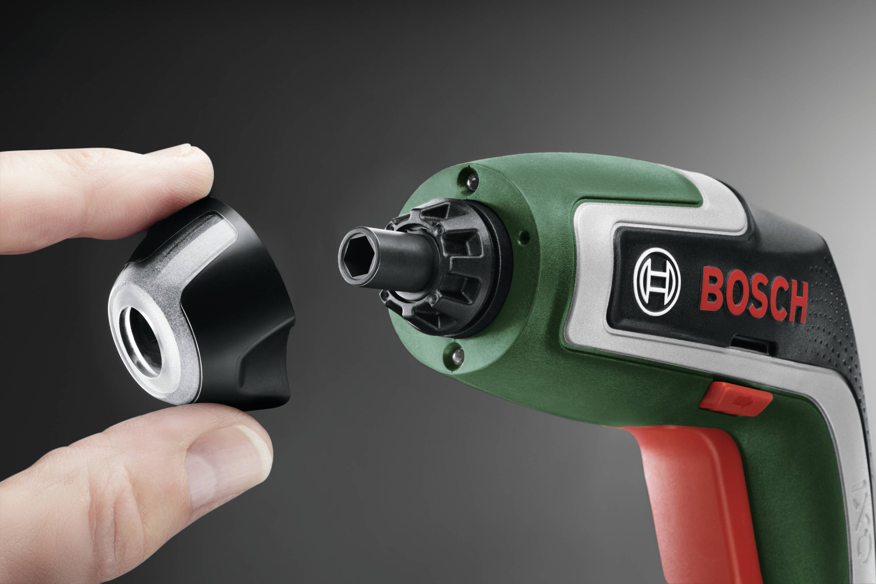 Een groene en rode Bosch-boormachine met verwisselbare boorkop wordt door een hand vastgehouden en gepresenteerd.