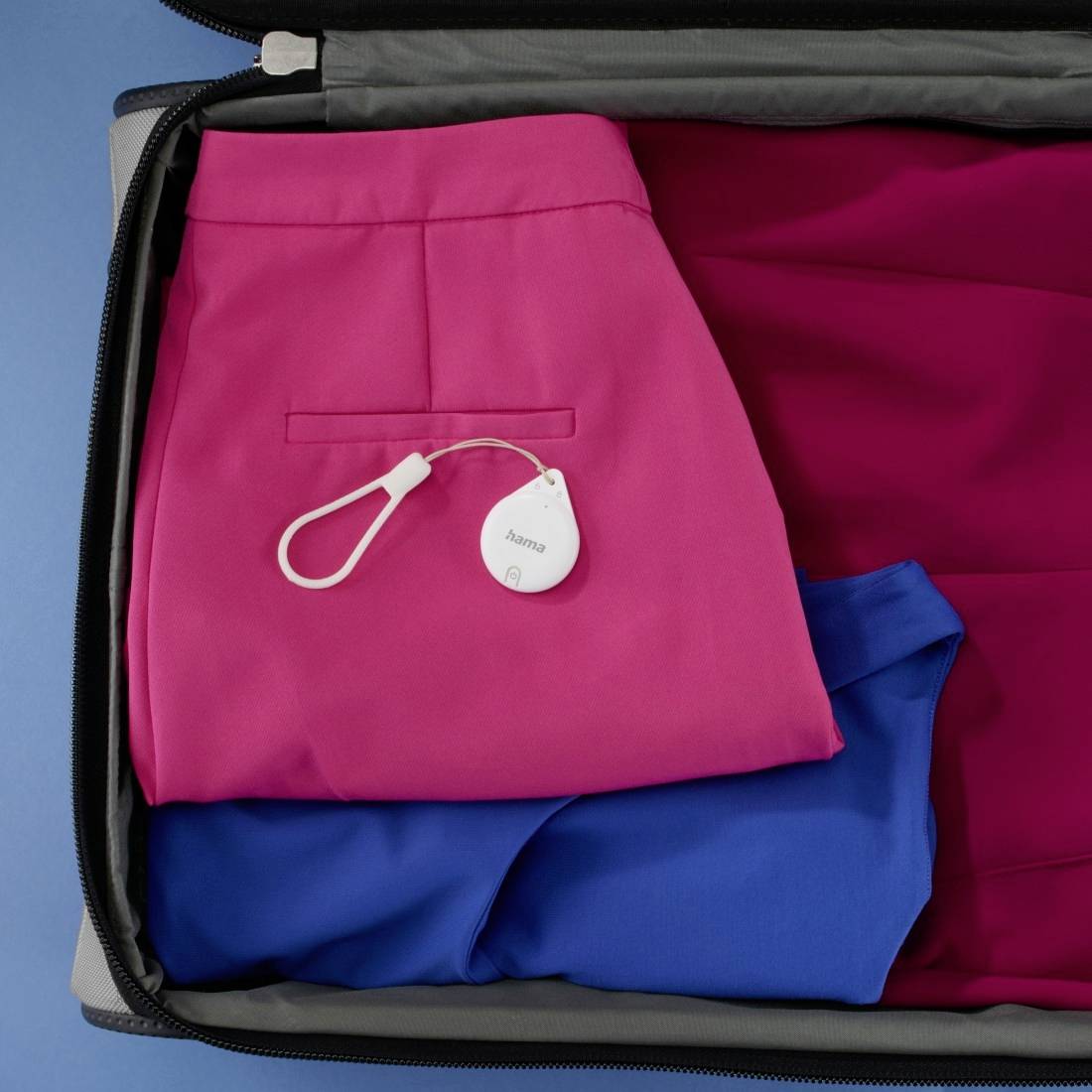 Een koffer met een roze broek en een blauw shirt, uitgerust met een witte, ronde tracker die aan de rand van de broekzak is bevestigd.