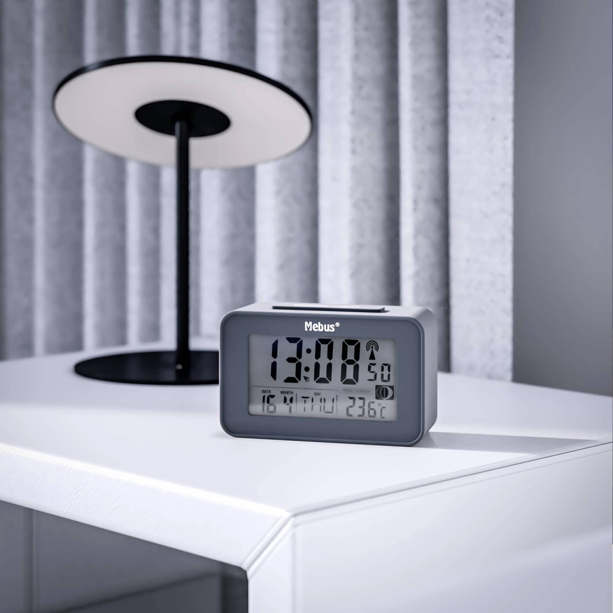 Een digitale wekker toont '13:08' en 'Zaterdag, 5 oktober'. Op de achtergrond staat een moderne, zwarte lamp op een witte tafel.