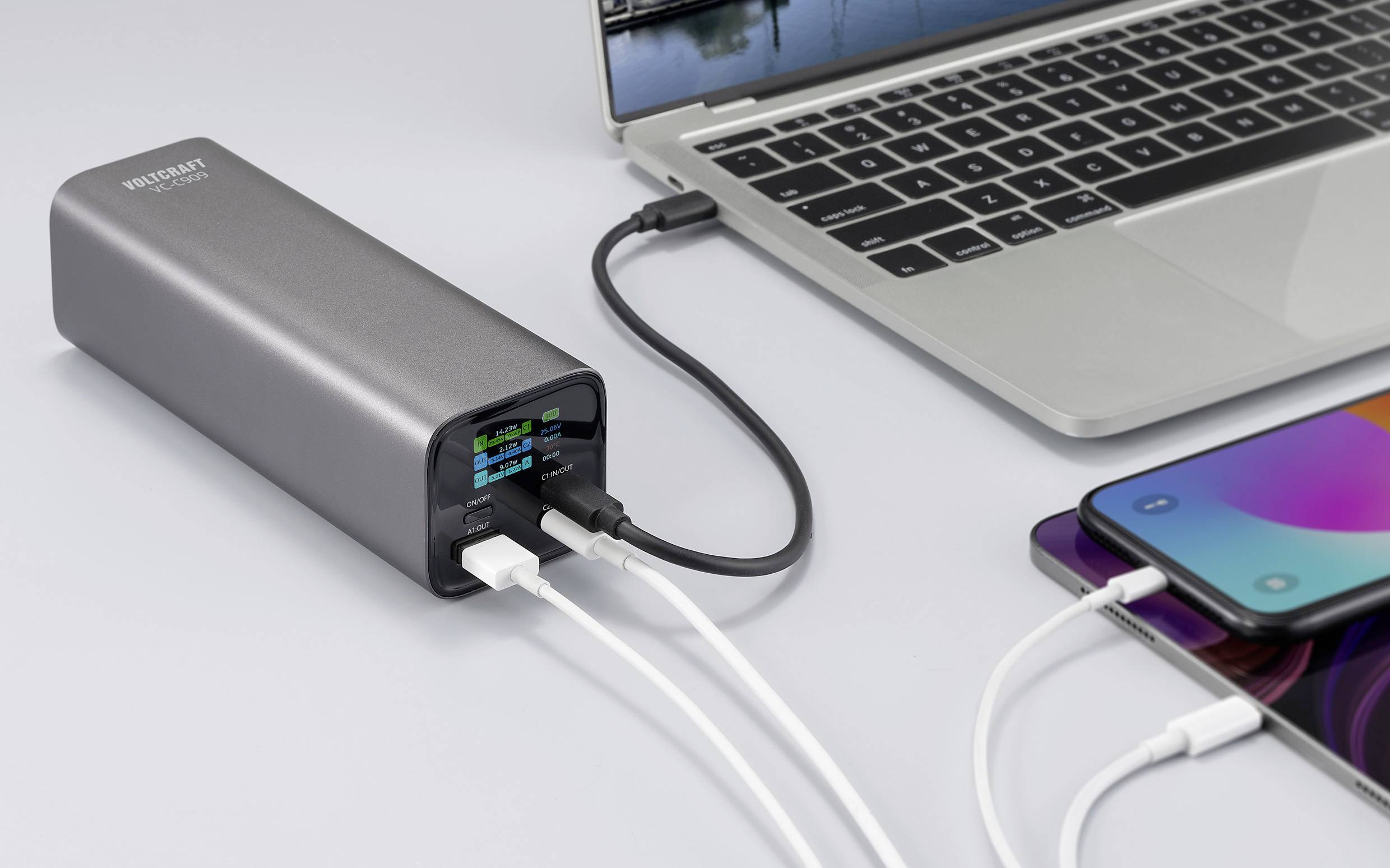 Een grijze powerbank laadt tegelijkertijd een laptop en een smartphone op. Er zijn verschillende kabels aangesloten.