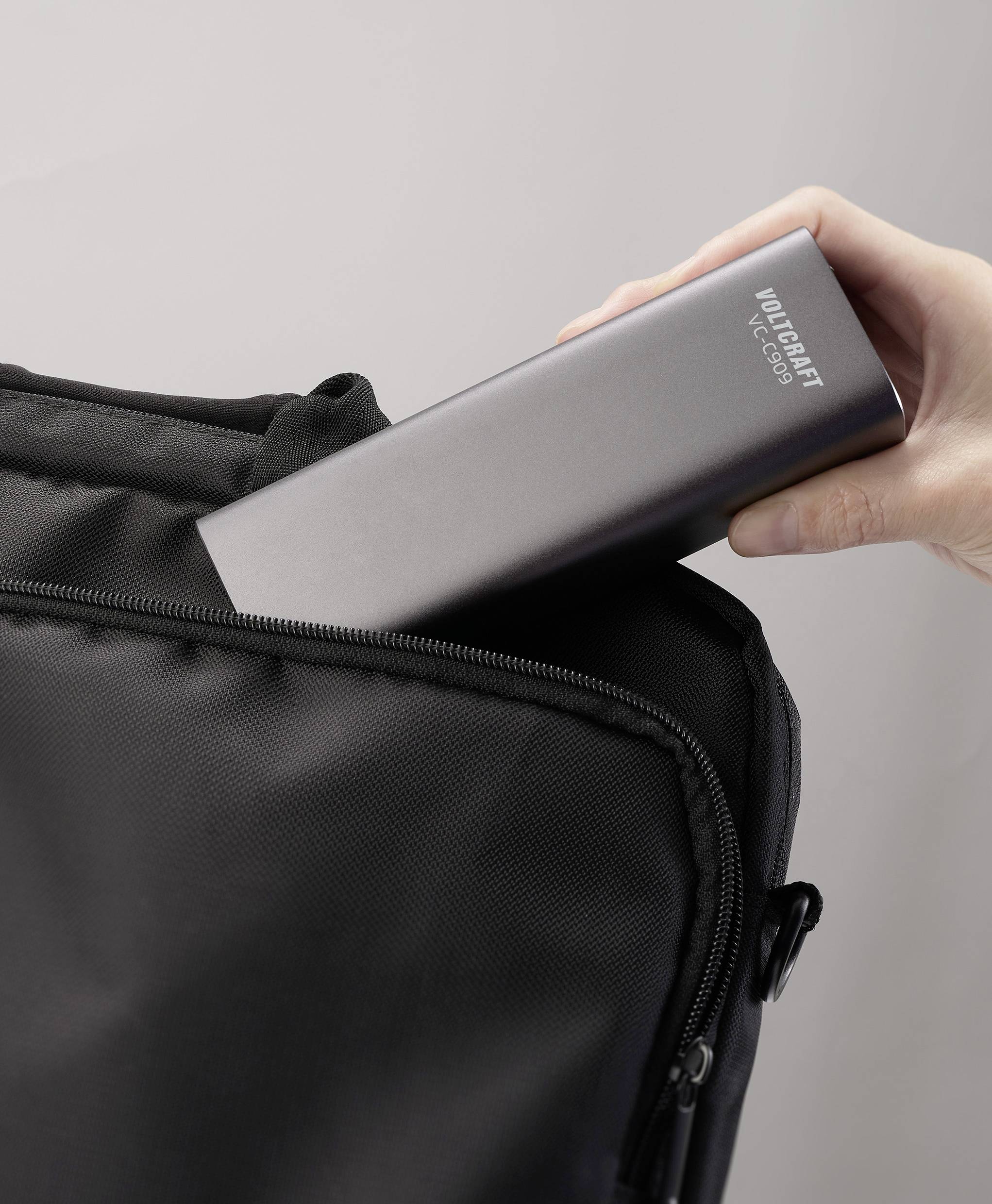 Een hand steekt een zwarte draagbare powerbank in een tas.