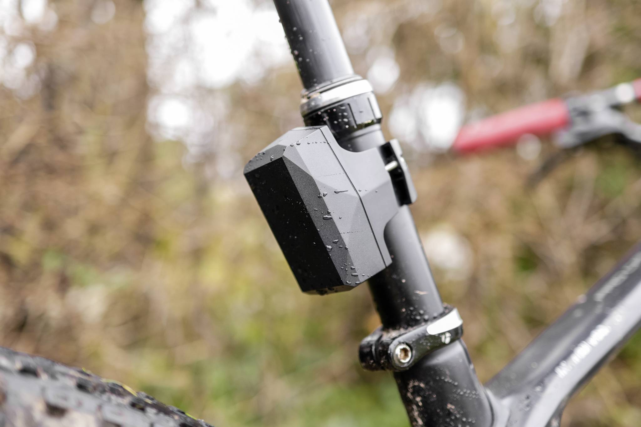 Close-up van een zwart-grijs fietsdeel aan een metalen frame. Vuil- en waterdruppels zijn zichtbaar. Achtergrond wazig.