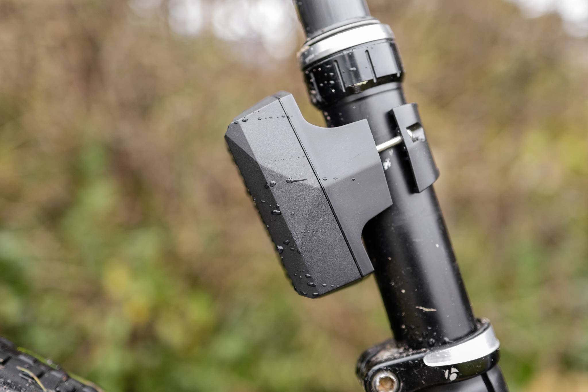 Een zwart fietslicht is bevestigd aan de zadelpen van een fiets. Op de achtergrond zijn wazig groene planten zichtbaar.