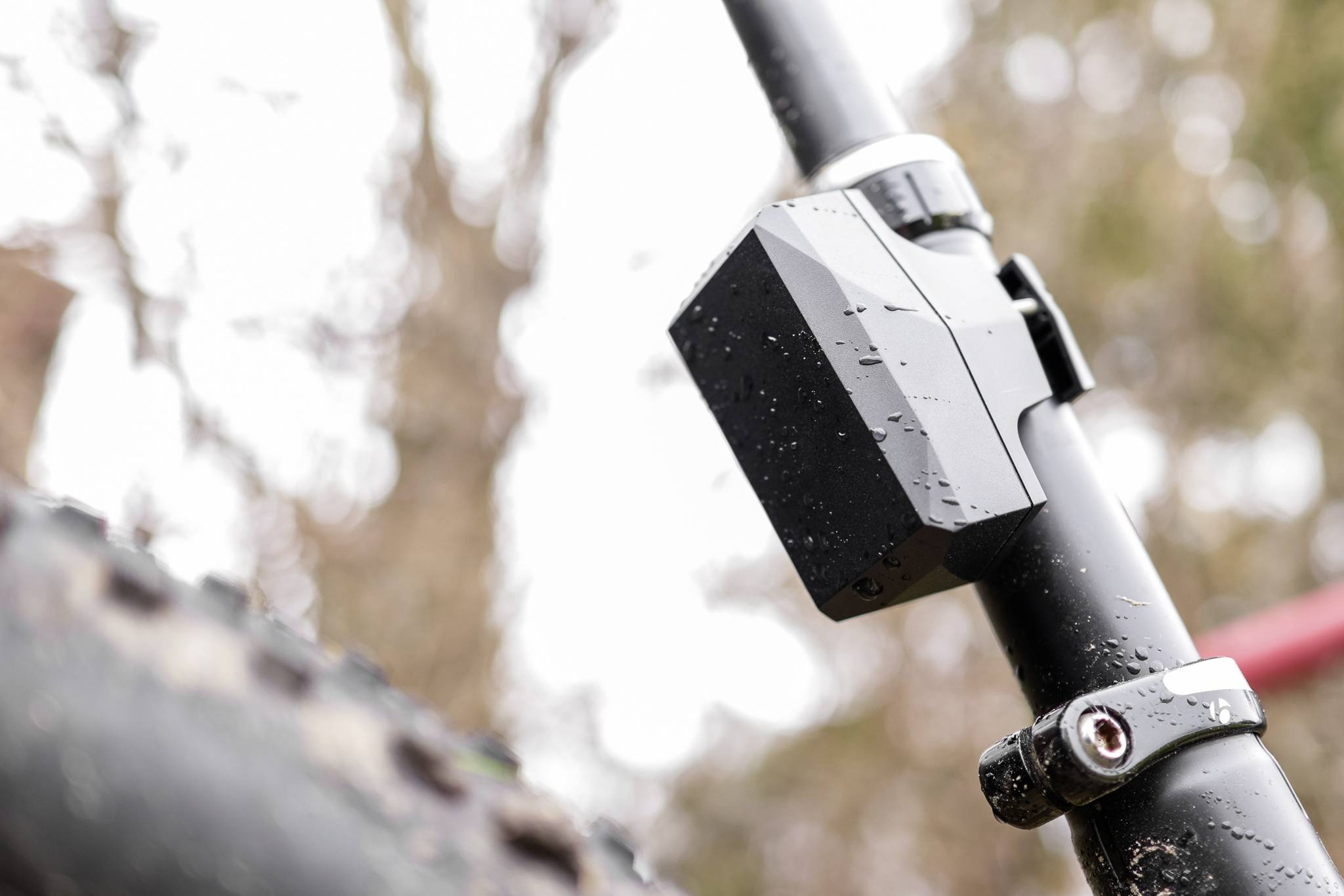 Close-up van een fietsframe met een gemonteerde doos en een modderige band; wazig herfstblad op de achtergrond.