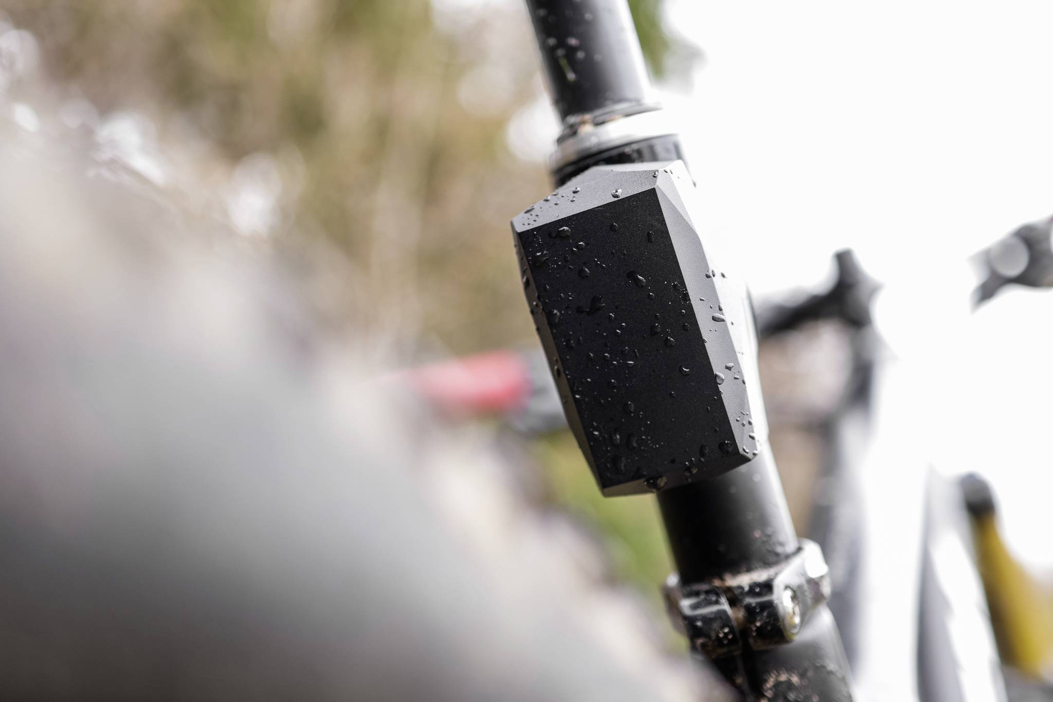 Close-up van een zwarte fietsvoorvork met waterdruppels. De achtergrond is wazig, een indicatie van regenachtig weer.