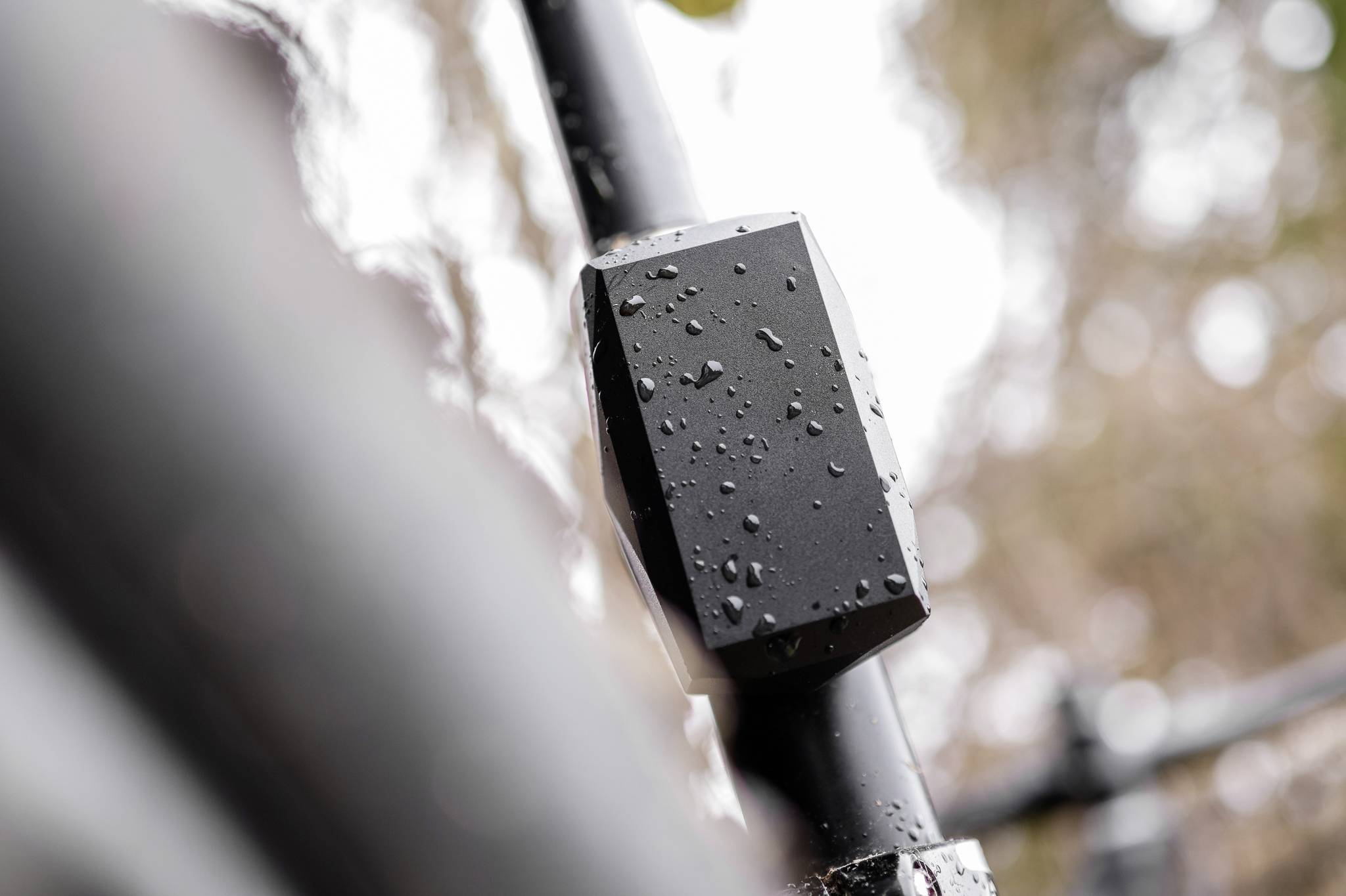 Een zwart, regennat object is bevestigd aan een stok. Onscherpe achtergrond met bomen. Weerbestendig apparaat in de buitenlucht.