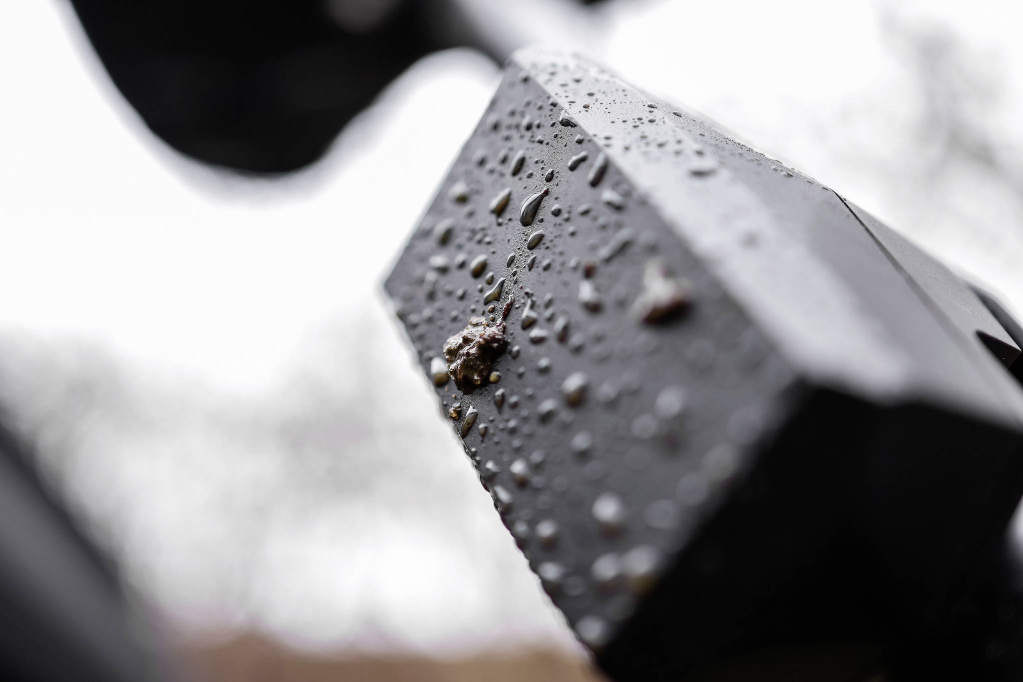 Close-up van een regennat oppervlaktestructuur van een buitenvoorwerp, mogelijk een behuizing of apparaat, met waterdruppels.