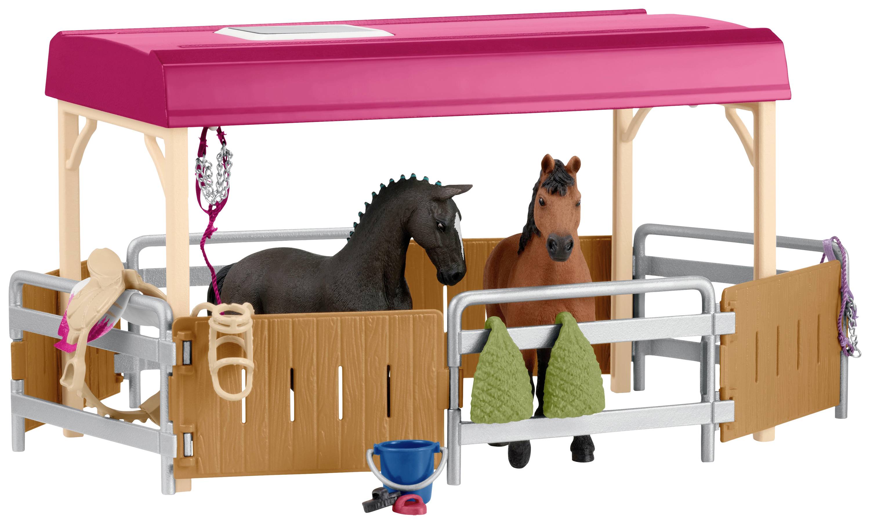 Twee plastic paarden staan in een speelgoed-paardenstal met een open dak. De stal heeft toebehoren zoals emmers, tuig en zadel.