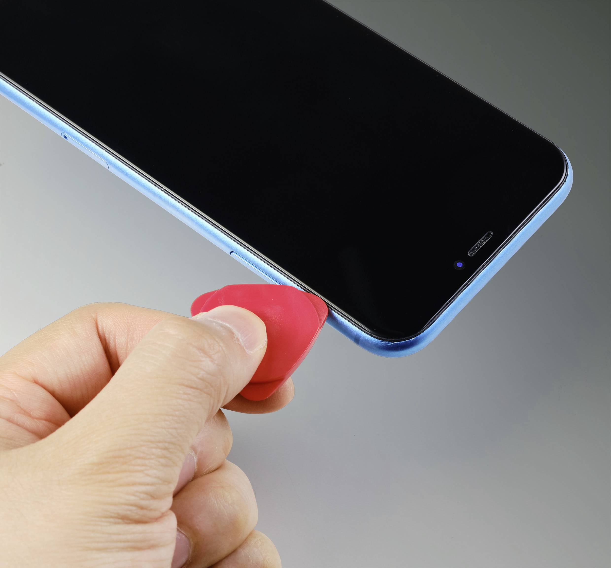 Een persoon gebruikt een rood kunststof gereedschap om een smartphone te openen. De mobiele telefoon is blauw en wordt aan de zijkant bewerkt.