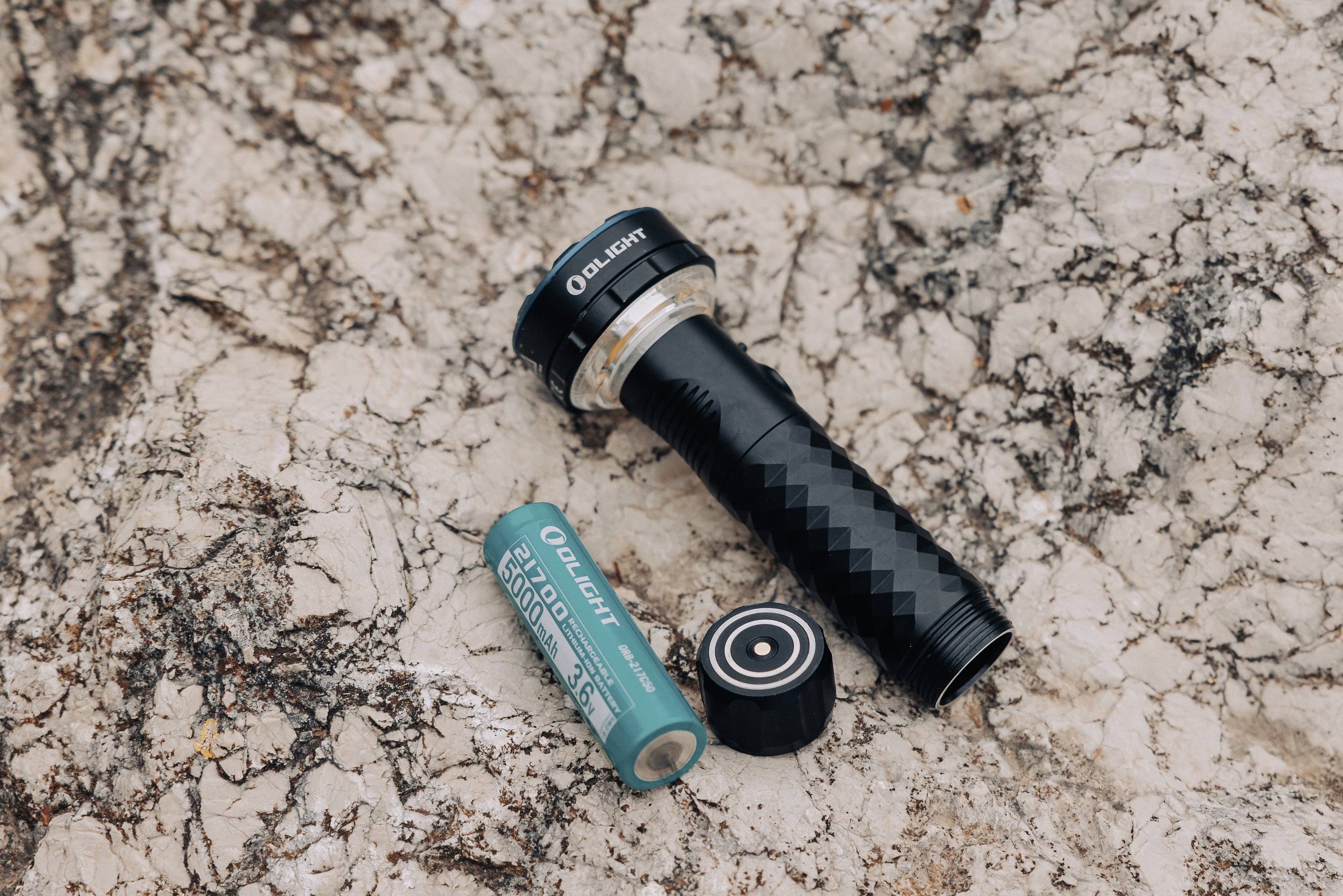 Zwarte zaklamp zonder kap ligt met verwijderde batterij op een stenig oppervlak.