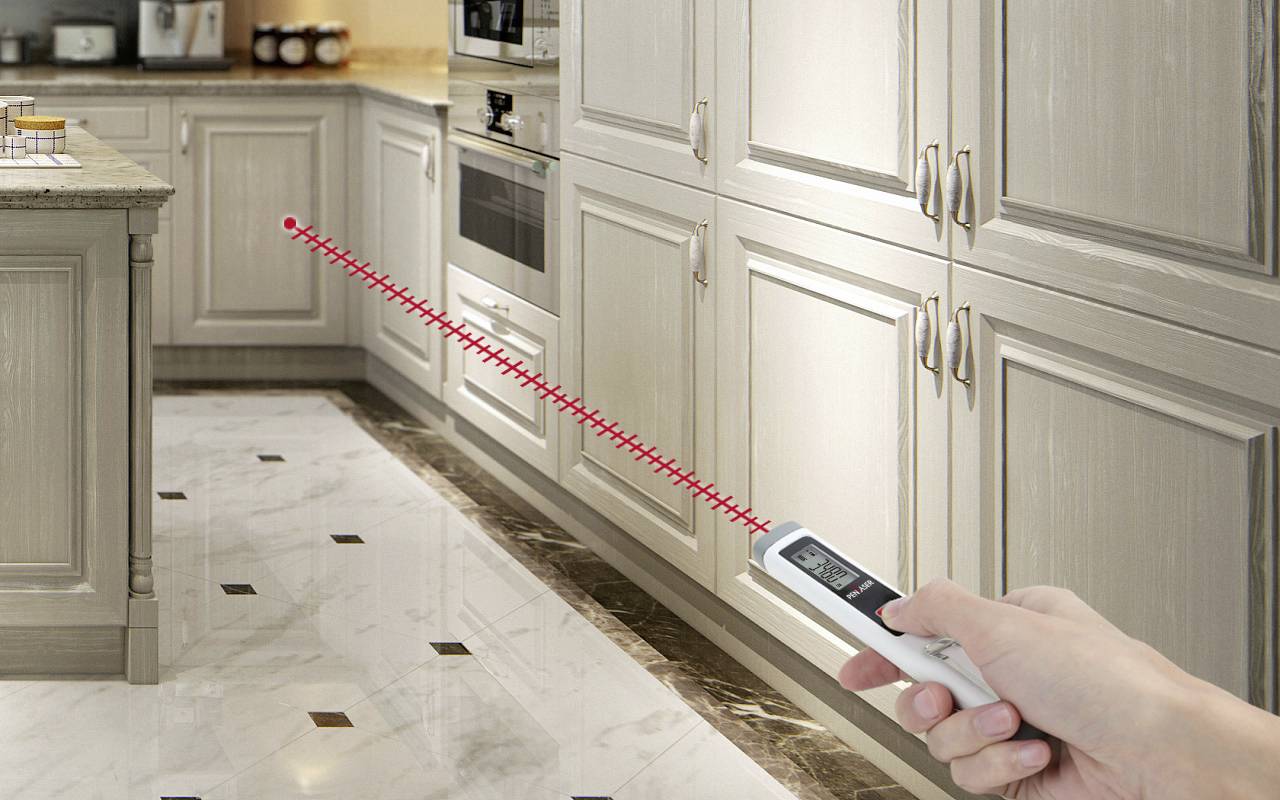 Een hand houdt een afstandsmeter vast die gericht is op keukenkastjes. De rode laserstraal toont de afstandsmeting.