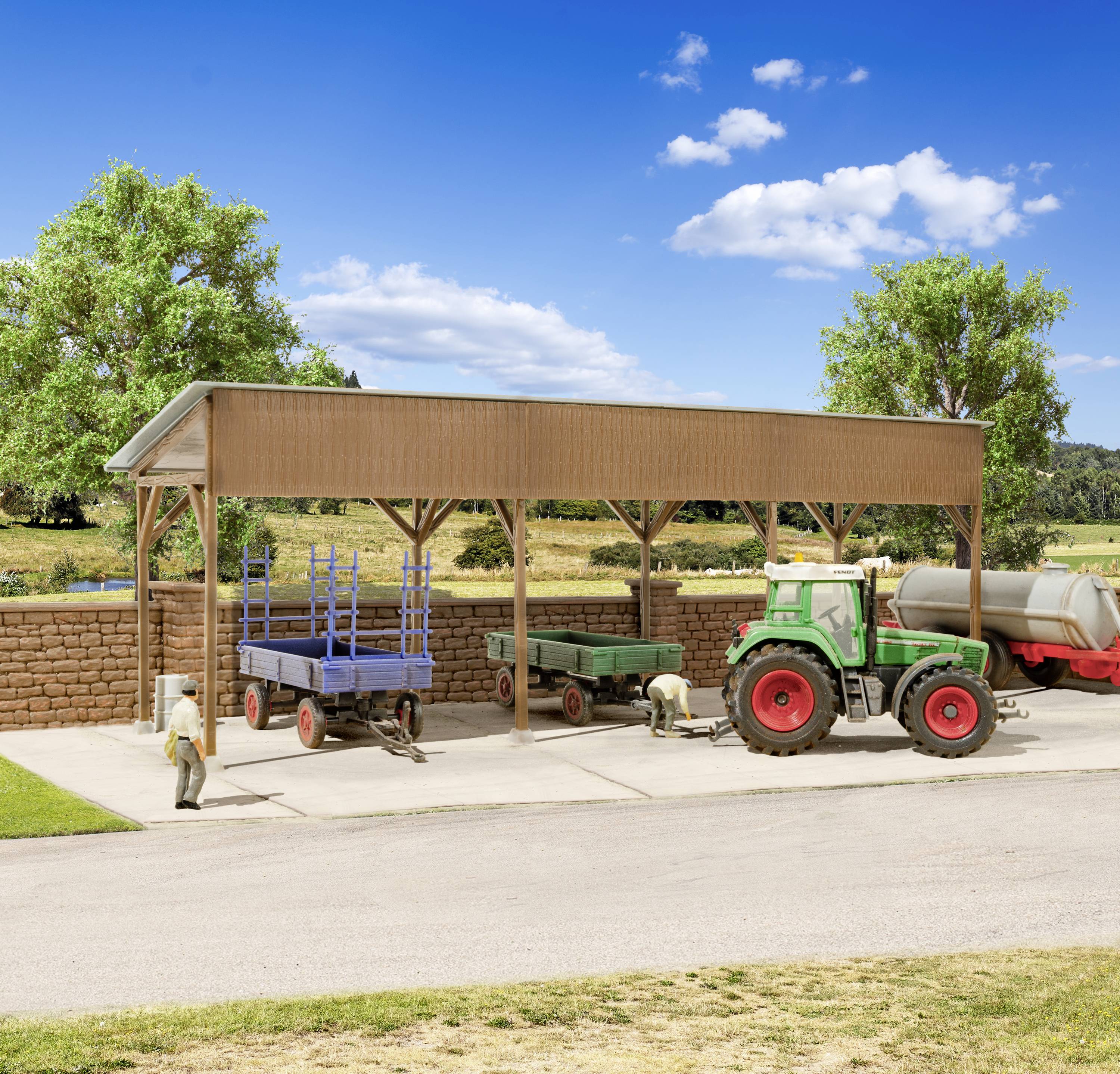 Een rode tractor staat onder een schuur op een boerderij, omringd door landbouwmachines en twee bomen op de achtergrond.
