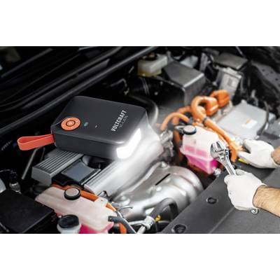 Een persoon repareert een motor. Een draagbaar starthulpapparaat verlicht de motorruimte.