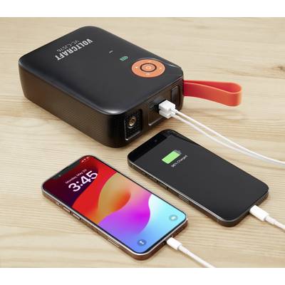 Een draagbare oplader laadt twee mobiele telefoons op een houten tafel. Een mobiele telefoon toont een tijdstip, de andere toont een volle batterij.