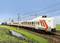 Een witte trein met rode strepen rijdt over een spoor door een groene landschap, met een blauwe lucht op de achtergrond.