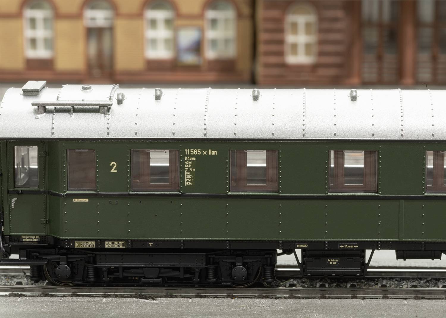Een donkergroene historische spoorwagen met het opschrift '11565 Klan' staat op rails voor een achtergrond met rood-bruine gebouwen.