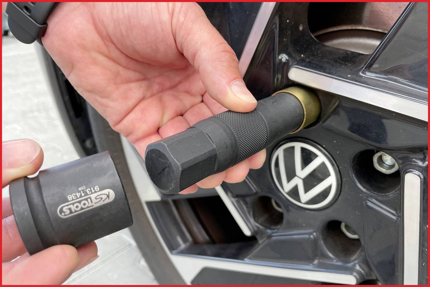 Twee handen verwisselen een autoband: Eén hand houdt een wielsleutel vast, de andere een adapter aan een zwarte velg.