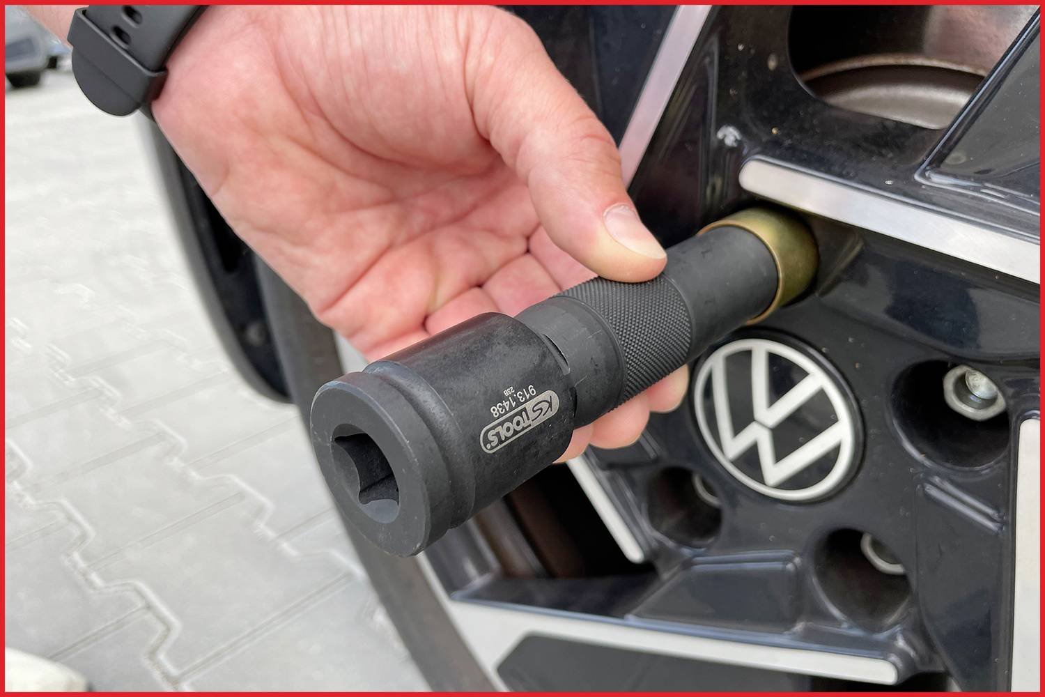 Een hand houdt een momentsleutel vast en draait een wielmoer strak op een autovelg met een VW-logo.