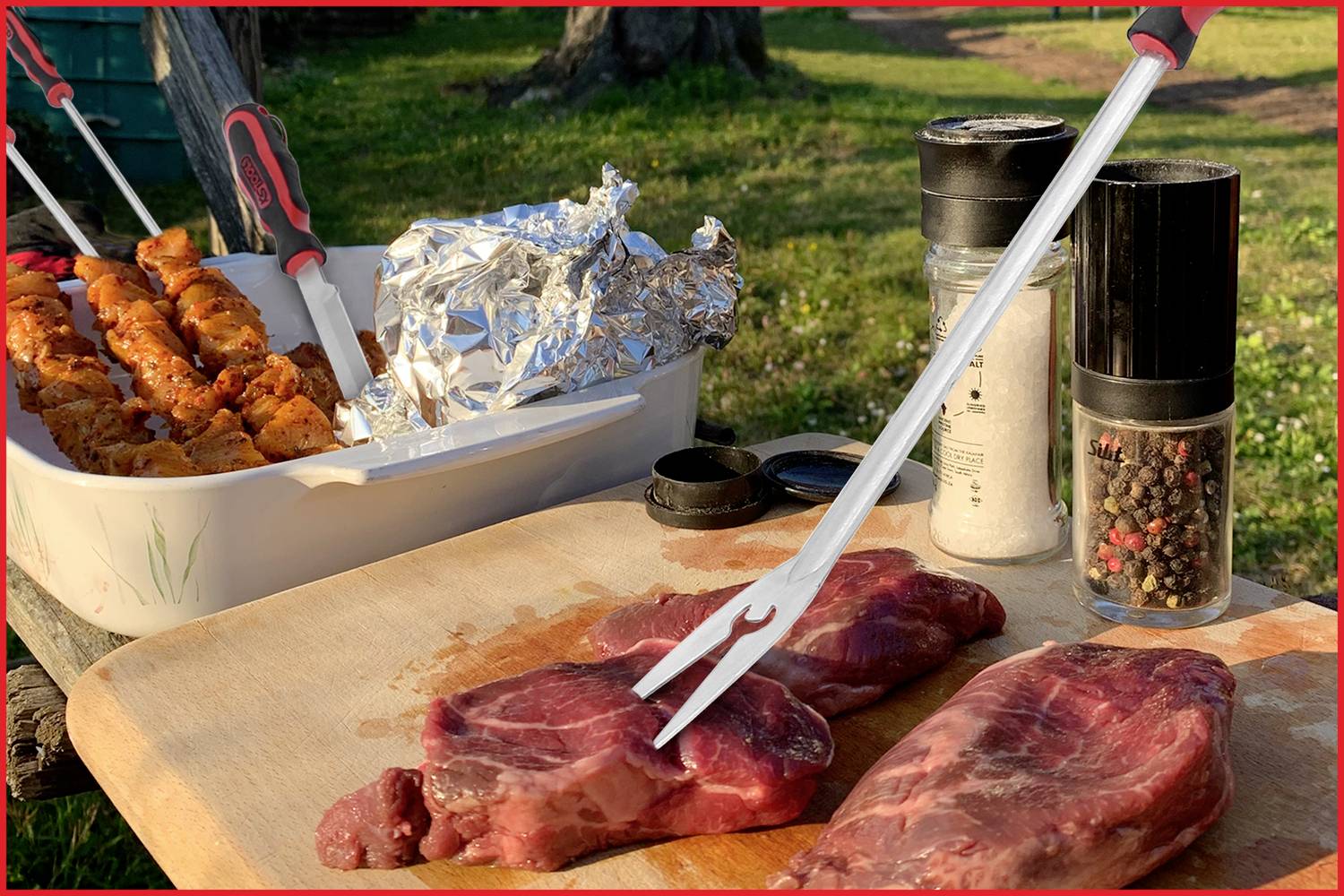 Een houten tafel buiten met rauw vlees, een vleeshaak, kruiden en voorbereide grillspiesjes op een grillplateau.