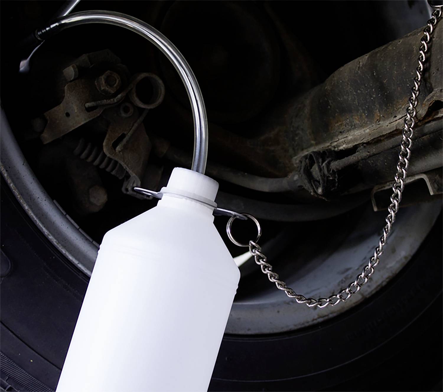 Witte oliekan met metalen ketting. Hij is aan een auto bevestigd en wordt gebruikt voor het smeren van voertuigonderdelen.