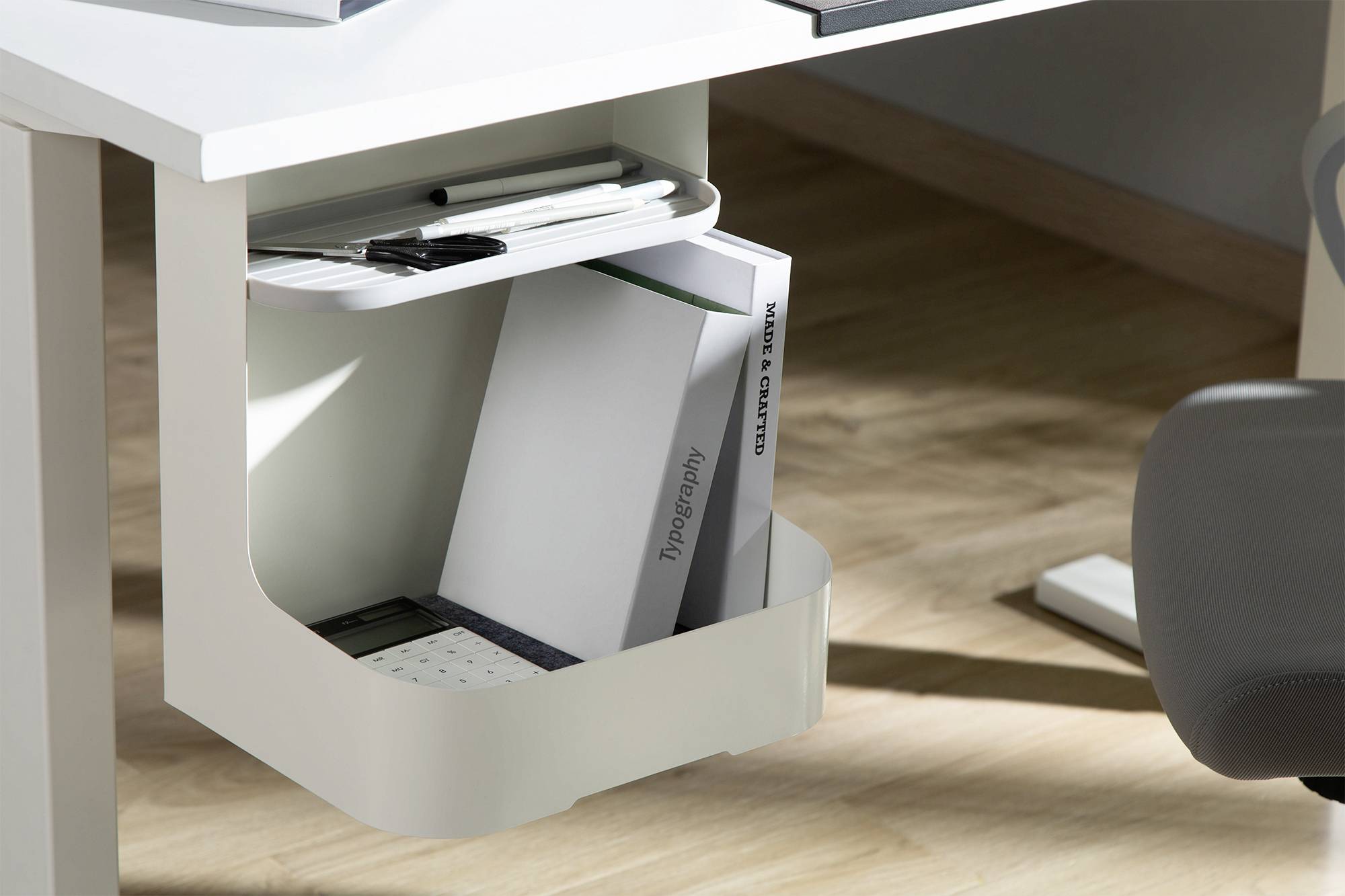 Boeken en schrijfbenodigdheden zijn netjes georganiseerd in een wit opbergvak onder een moderne bureautafel.
