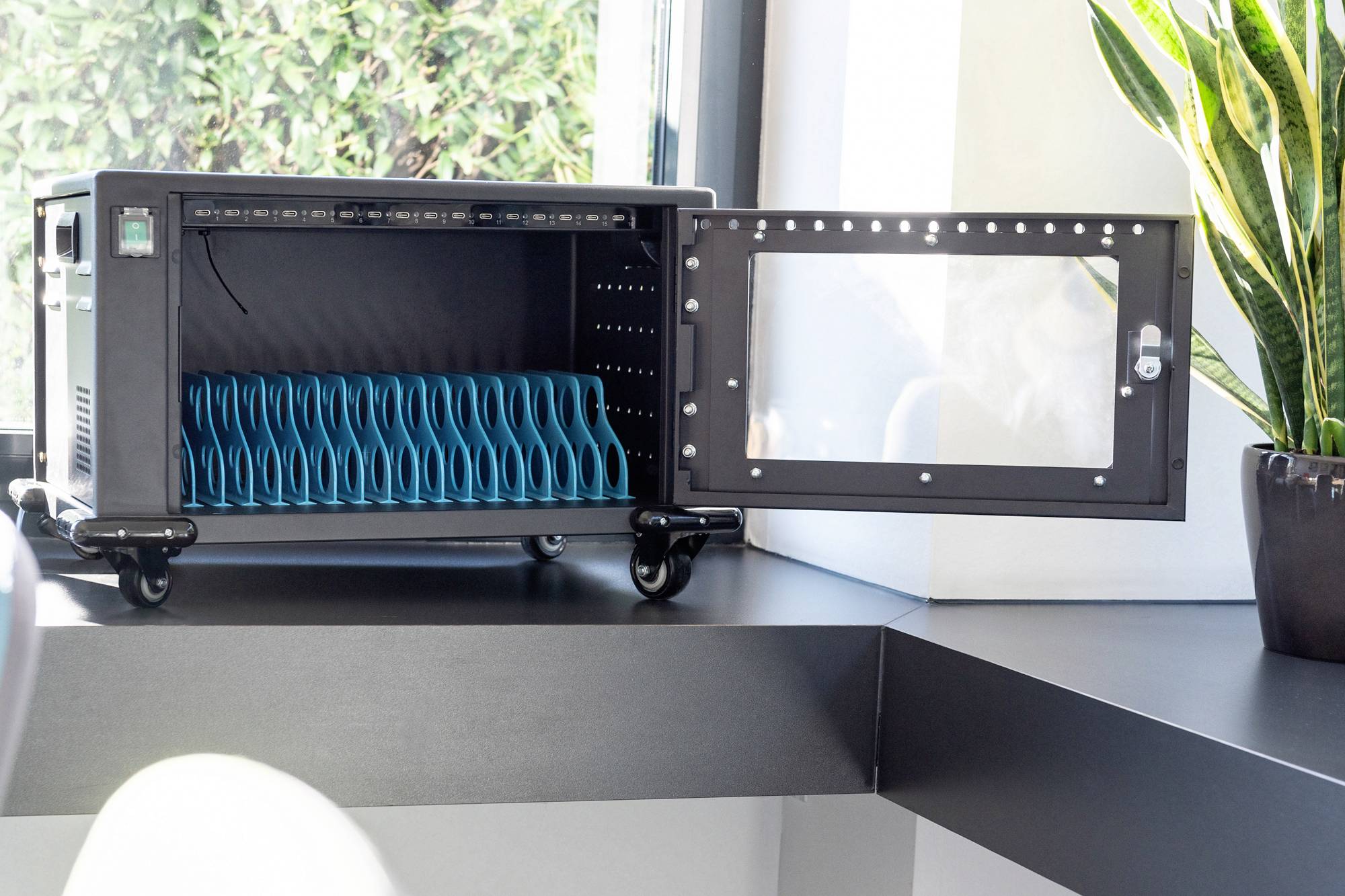 Een geopende laadwagen met meerdere tablets op een tafel. Een plant staat rechts ernaast, een raam links op de achtergrond.
