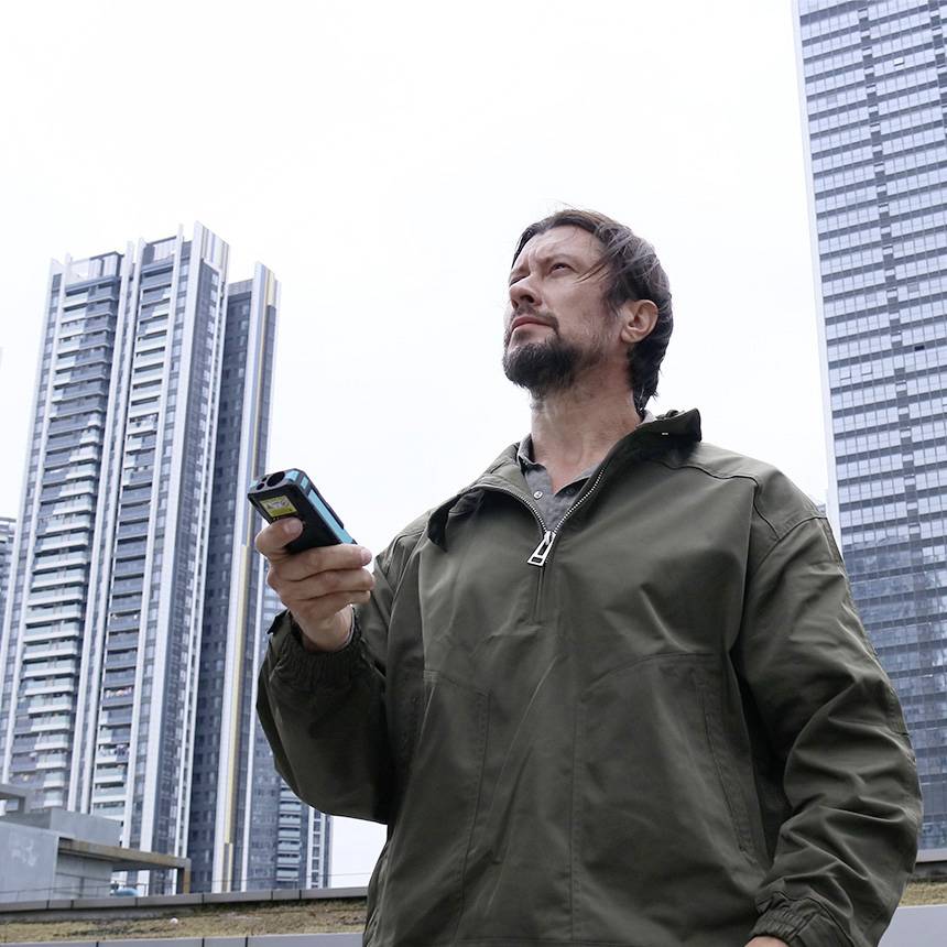 Een man buiten die een smartphone vasthoudt, met wolkenkrabbers op de achtergrond. Hij draagt een khakileren jas.