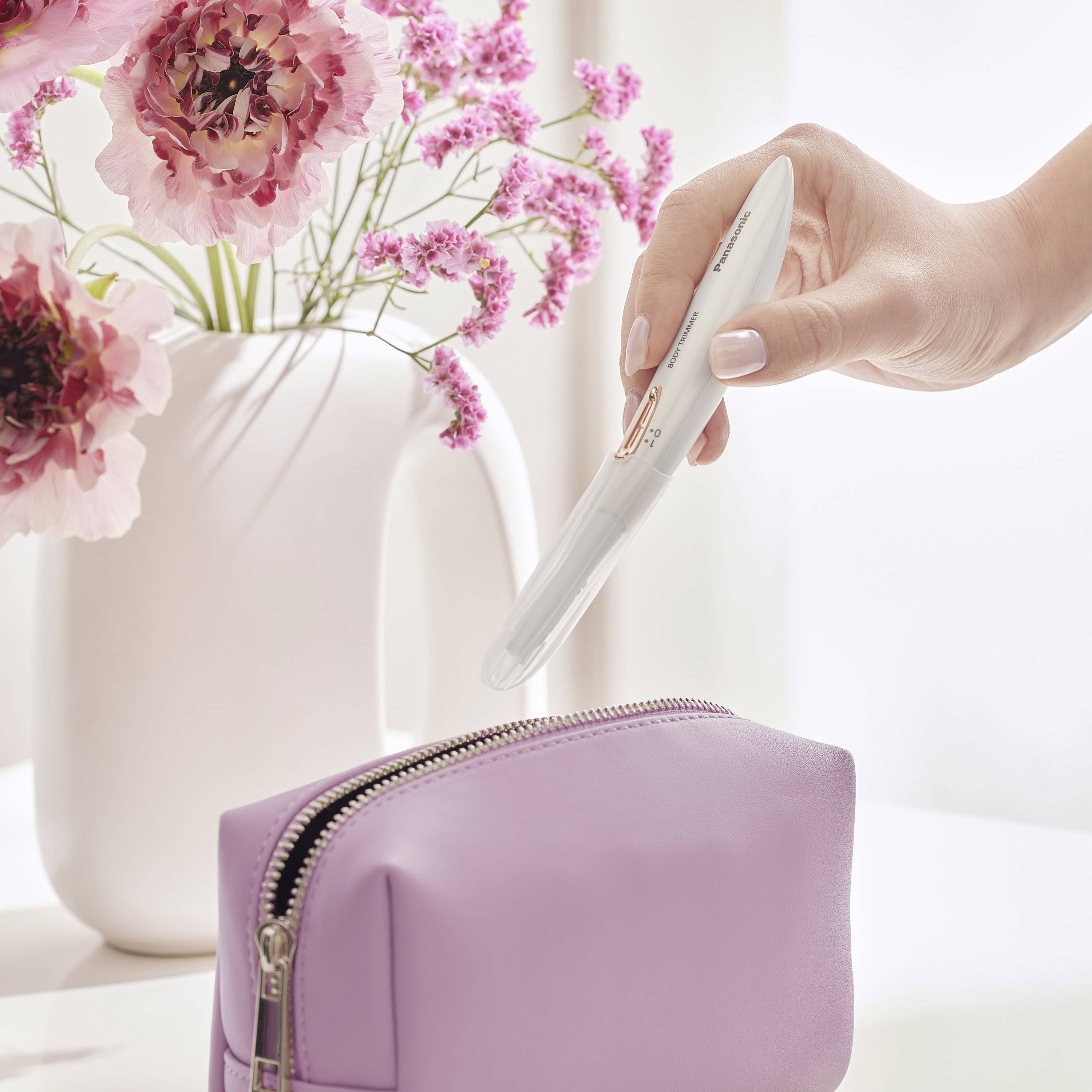 Een hand houdt een zwangerschapstest vast boven een paarse tas, met roze bloemen in een witte vaas op de achtergrond.