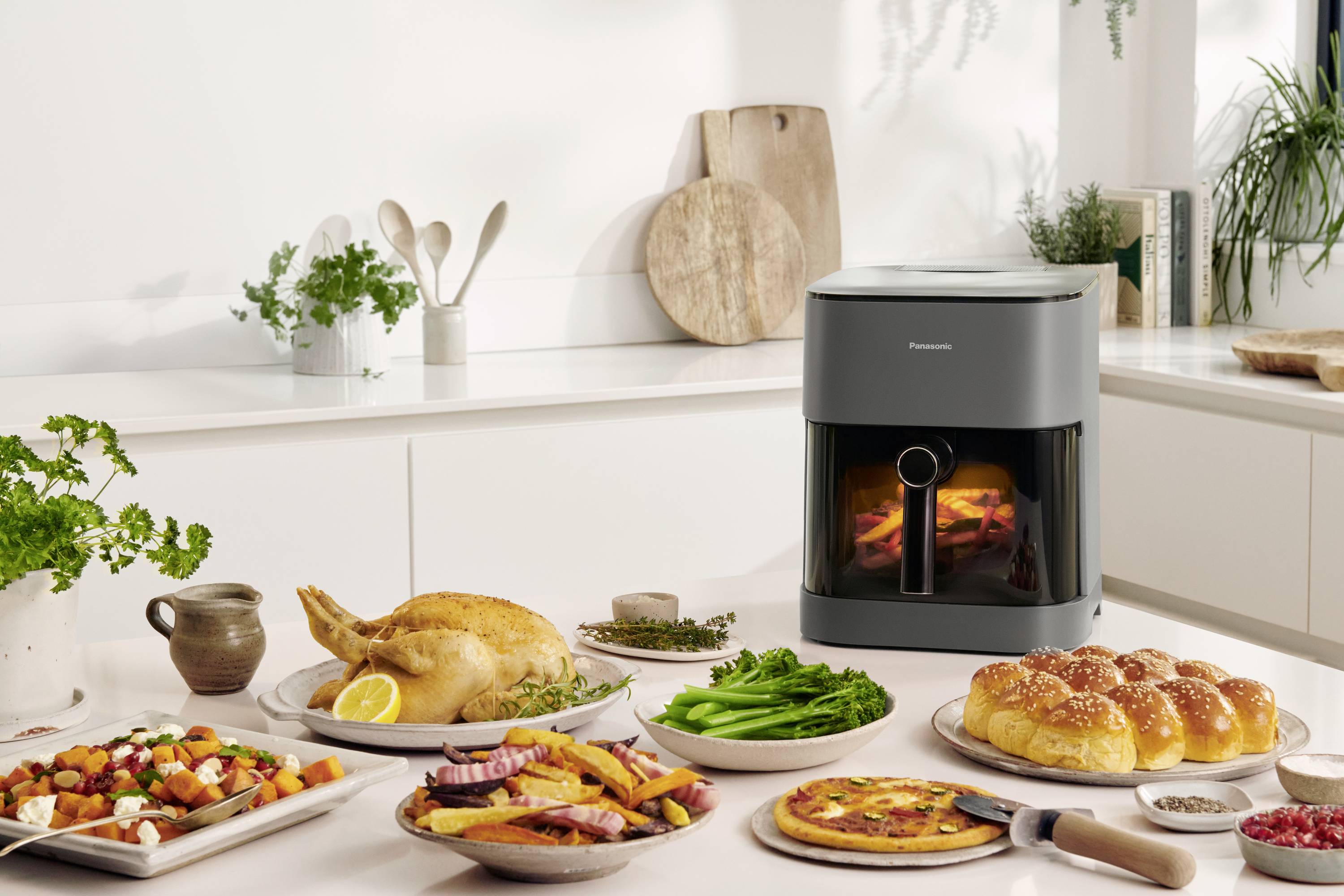 Een keuken met een moderne oven op het aanrecht. Op tafel staan verschillende gerechten, waaronder een gebakken kip, salade en brood.