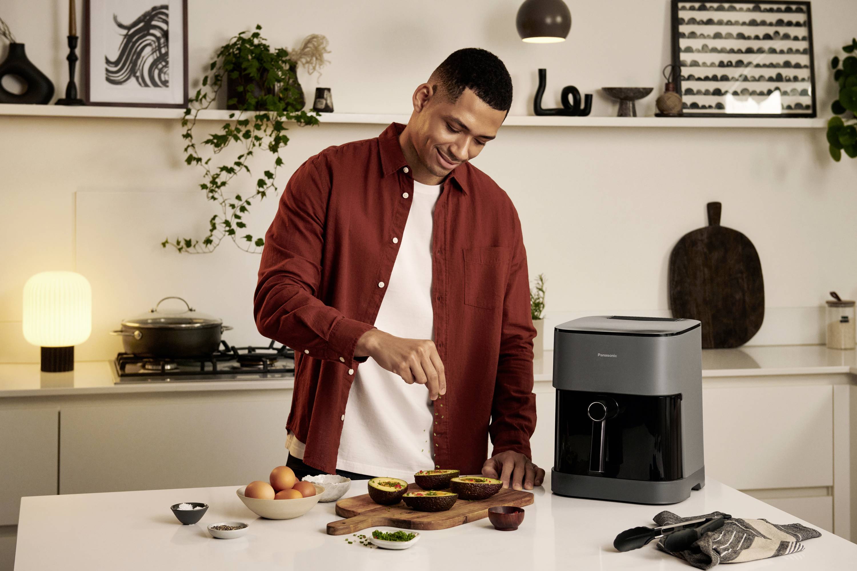 Een man bereidt maaltijden in een keuken met een modern airfryer-apparaat. Op het aanrecht liggen gesneden vruchten.
