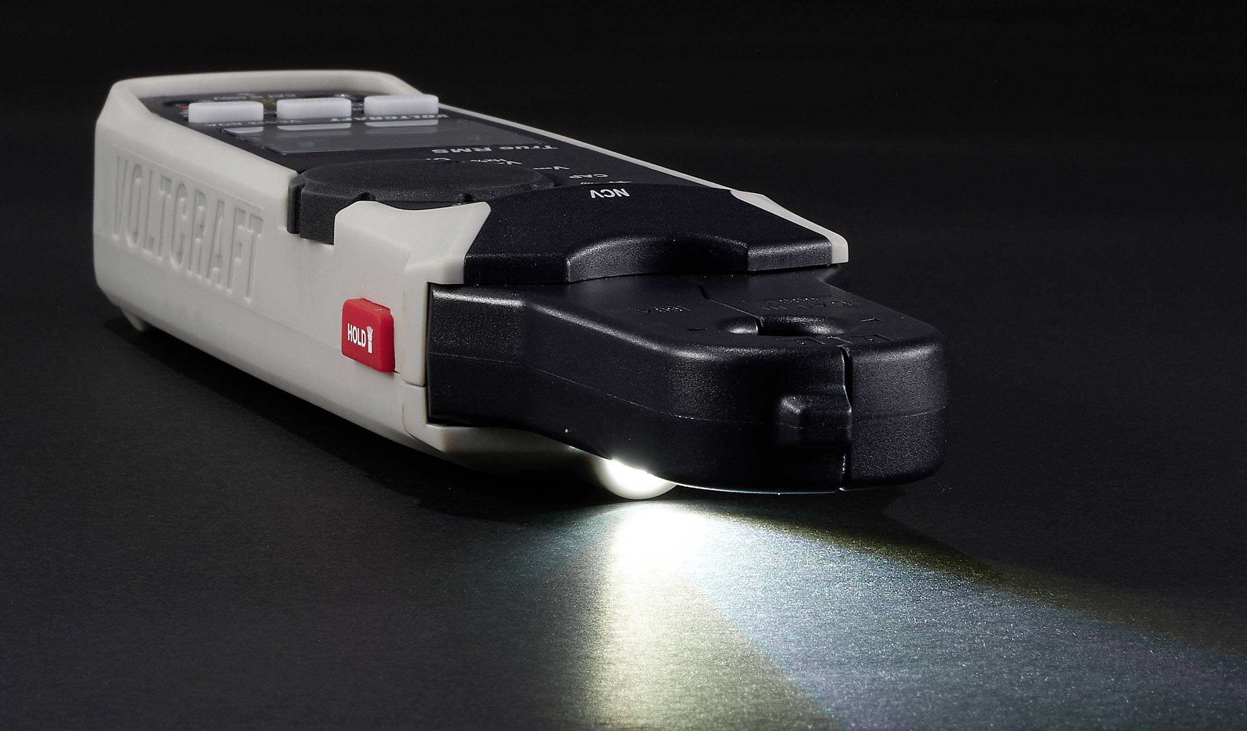 Een handgehouden multimeter op een donker oppervlak met een verlicht display, die meetmogelijkheden toont.